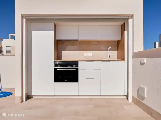 Blue Lake Penthouse | Espagne, Costa Blanca, Guardamar del Segura - appartement La cuisine extérieure se trouve derrière une porte roulante et dispose d’un accès à un four, une plaque de cuisson, une hotte aspirante, un réfrigérateur, un congélateur et un évier.