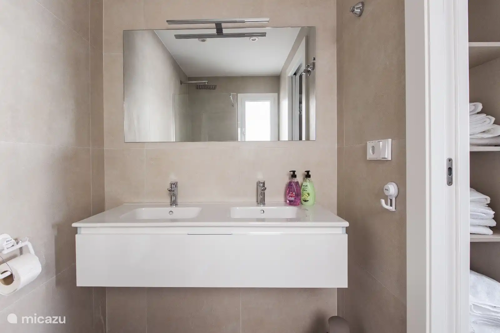 Cuarto de baño con ducha a ras de suelo, dos lavabos, inodoro, gel de ducha y secador de pelo.