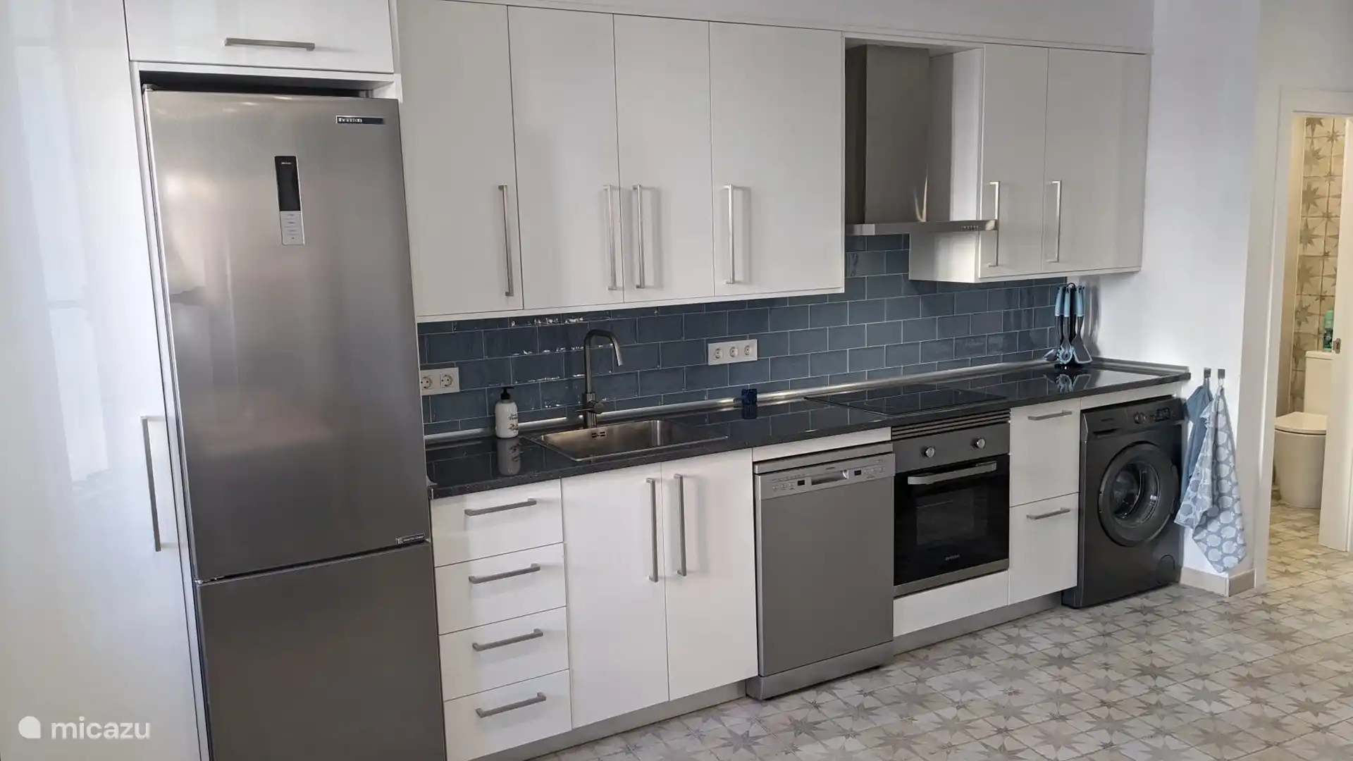 moderne Küche mit Induktionskochfeld, großem Kühlschrank, Geschirrspüler, Mikrowelle und Waschmaschine