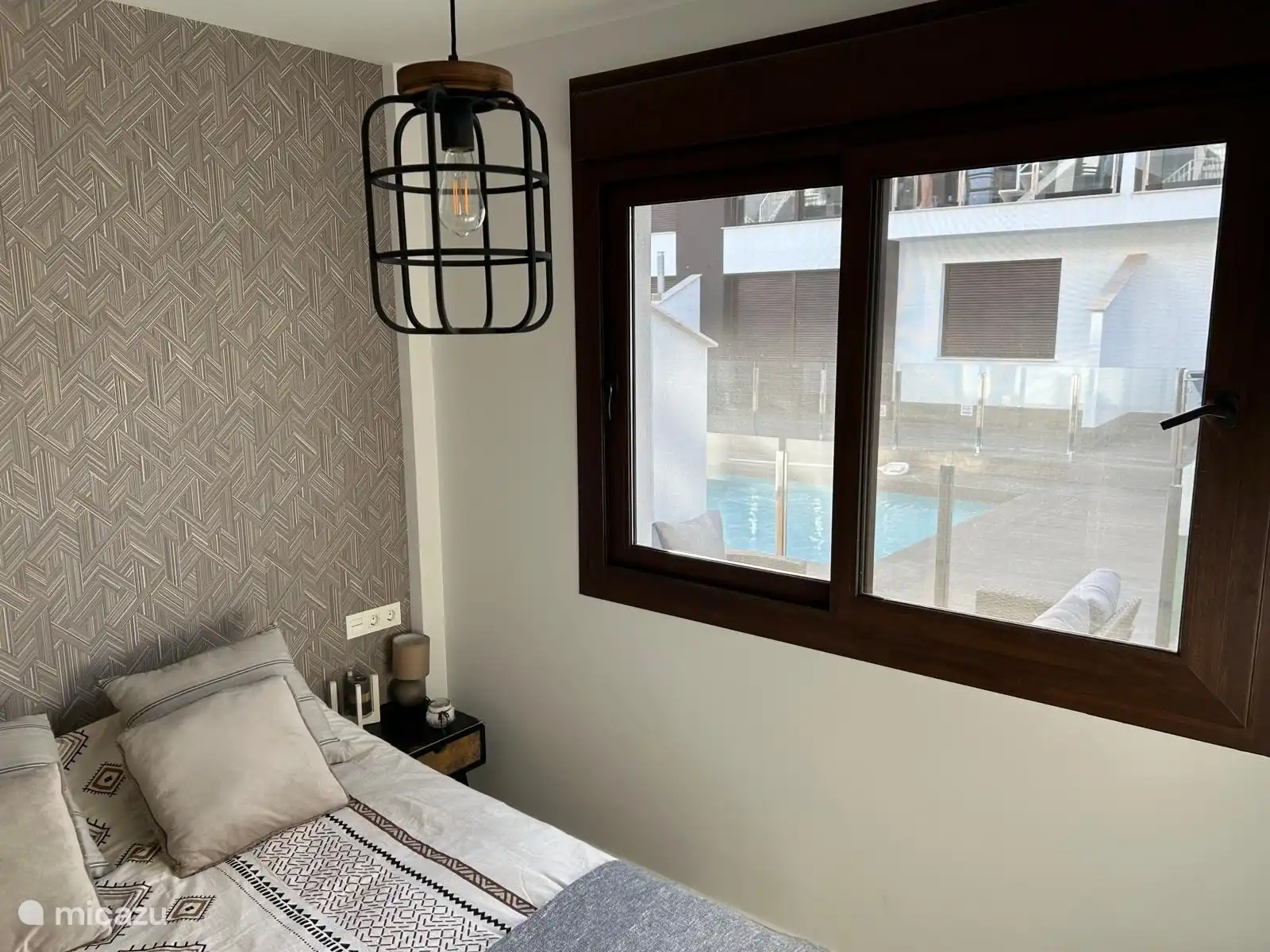 Großes Schlafzimmer mit Doppelbett, Blick auf den Pool, überall in der Wohnung sind Rollläden und Fliegengitter.