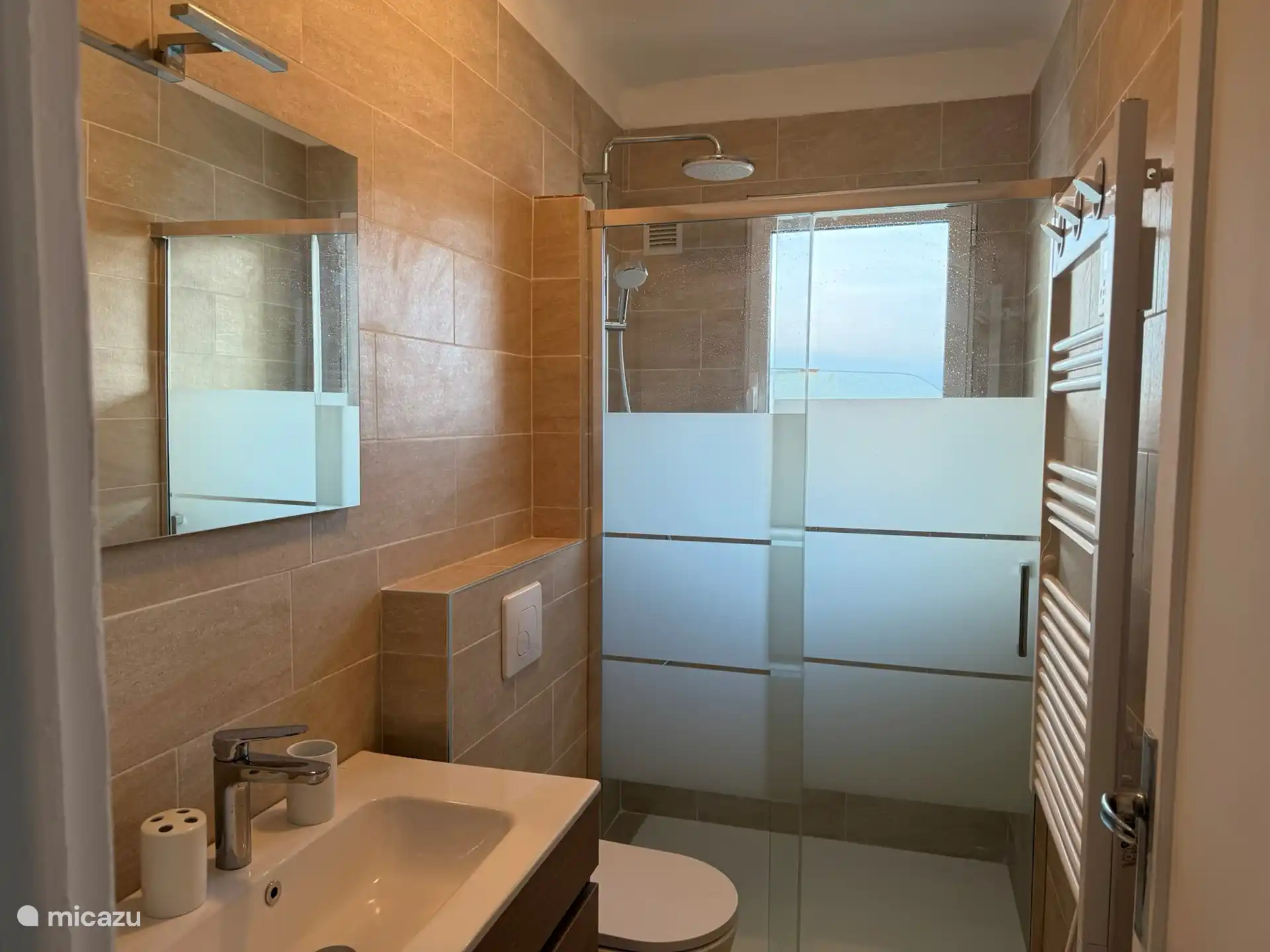 New bathroom from March 2025 with hot towel dryer, toilet, shower and sink.