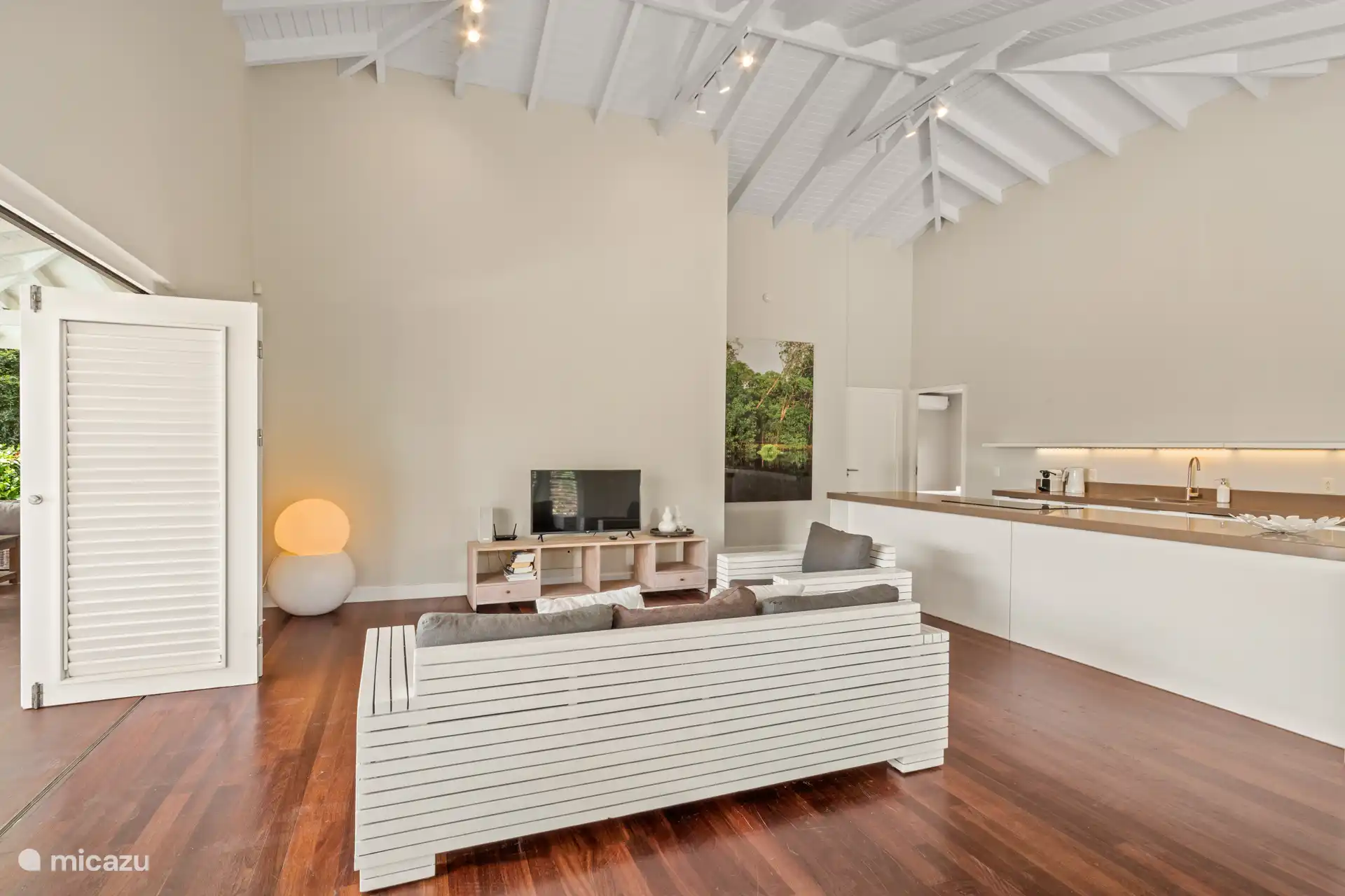 Tropische woonkamer met hoge plafonds, terrasdeuren en open keuken. De woning geeft je het echte binnen- buiten gevoel.