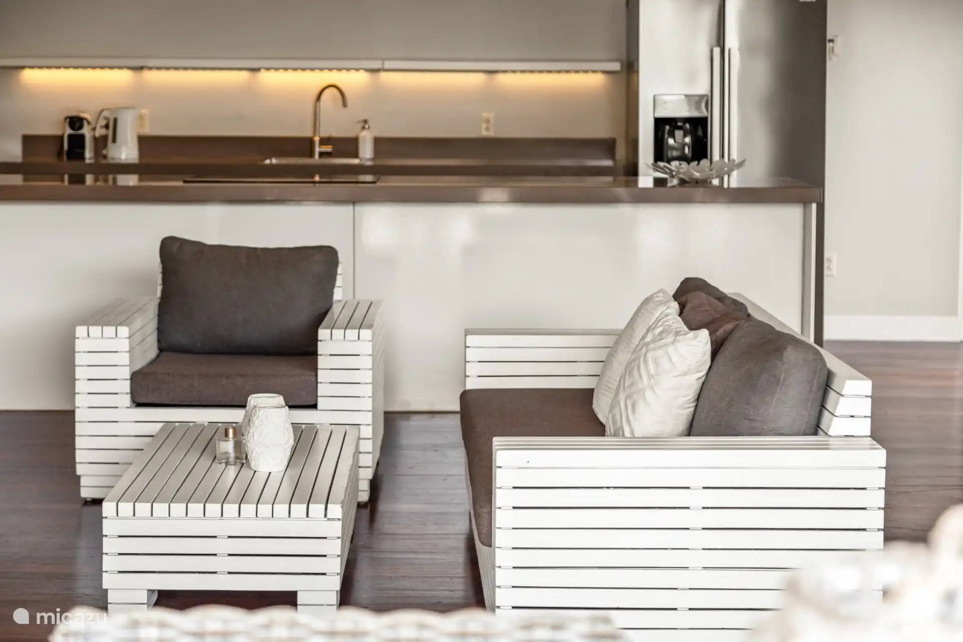 Tropische woonkamer met hoge plafonds, terrasdeuren en open keuken. De woning geeft je het echte binnen- buiten gevoel.