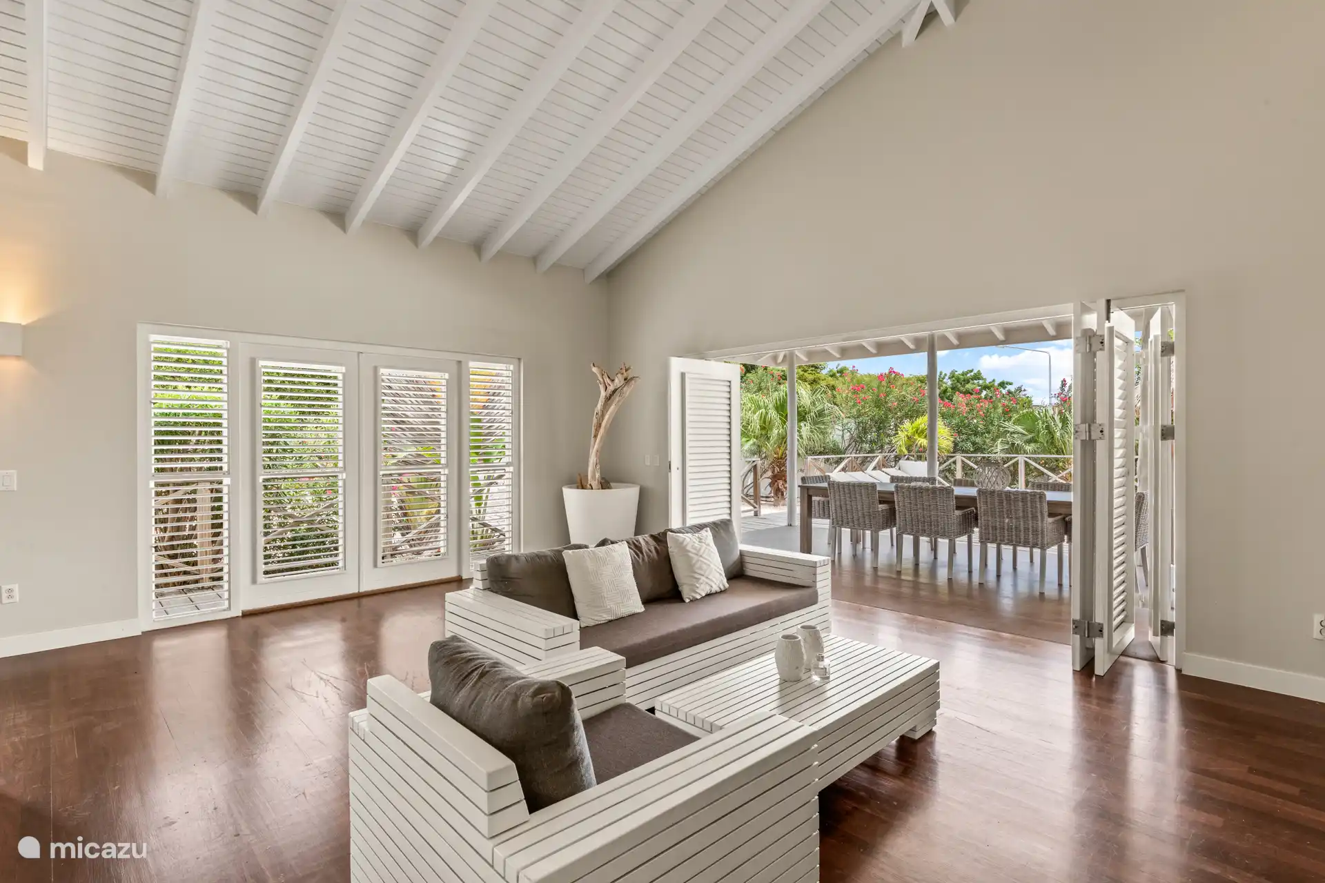 Tropische woonkamer met hoge plafonds, terrasdeuren en open keuken. De woning geeft je het echte binnen- buiten gevoel.