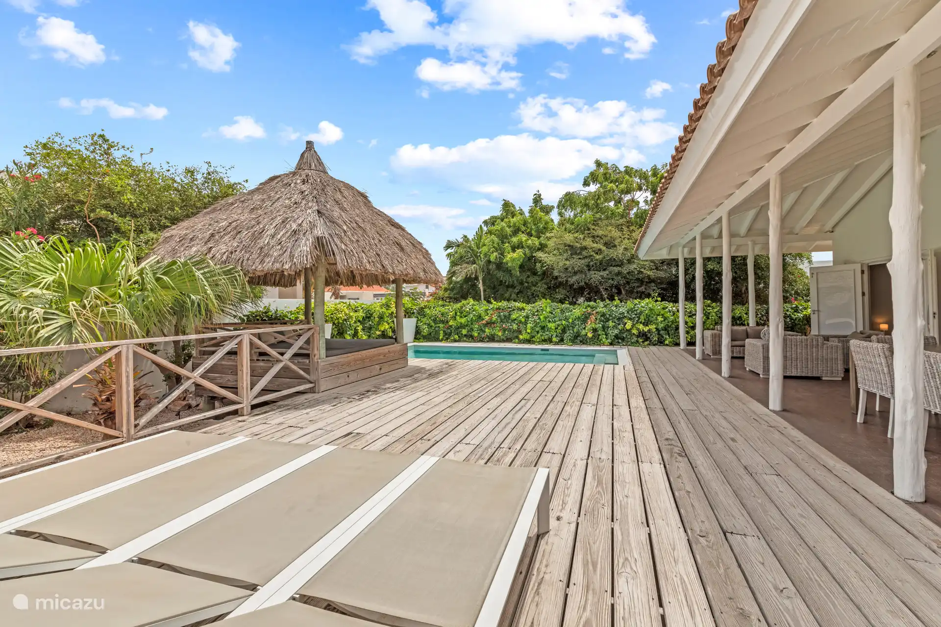 Als je de tuin inrijdt, stap je binnen in een paradijs. Kleurrijke bloemen, wuivende palmen, een zwembad met ligbedden, een palapa, een heerlijke loungeset en een grote eettafel buiten onder de verand