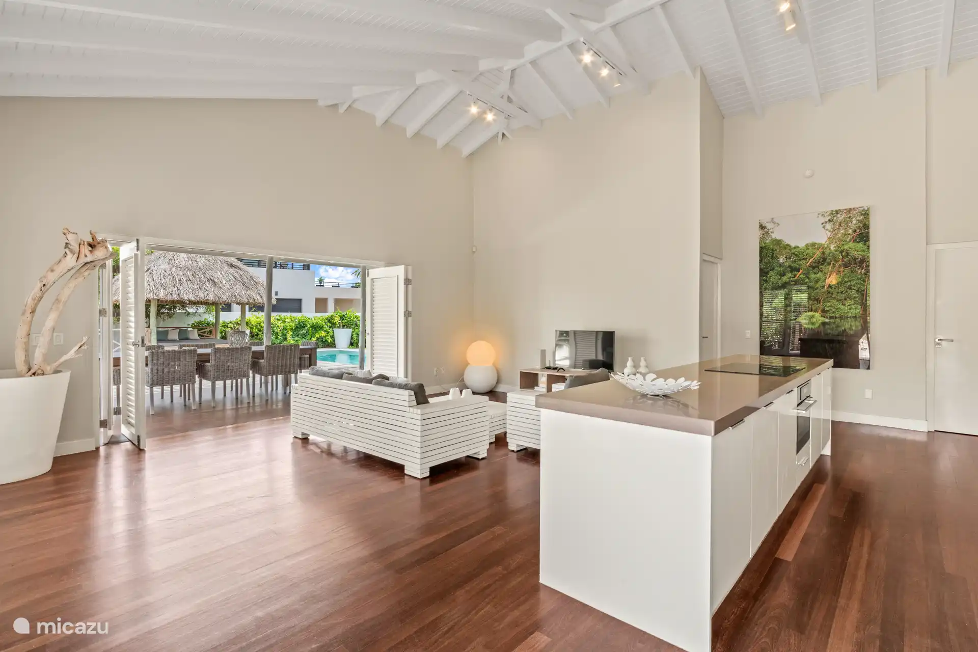 Tropische woonkamer met hoge plafonds, terrasdeuren en open keuken. De woning geeft je het echte binnen- buiten gevoel.