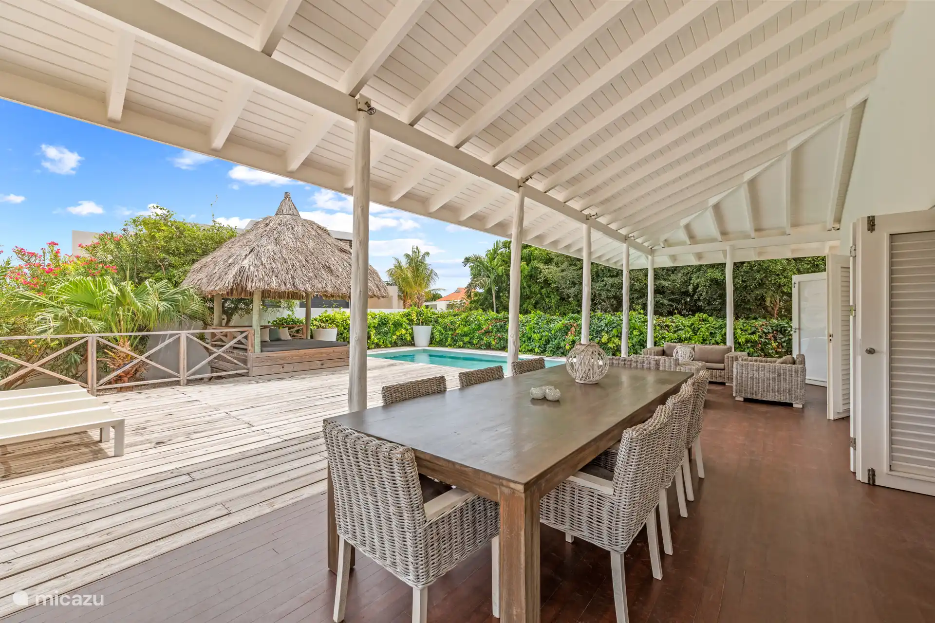 Als je de tuin inrijdt, stap je binnen in een paradijs. Kleurrijke bloemen, wuivende palmen, een zwembad met ligbedden, een palapa, een heerlijke loungeset en een grote eettafel buiten onder de verand