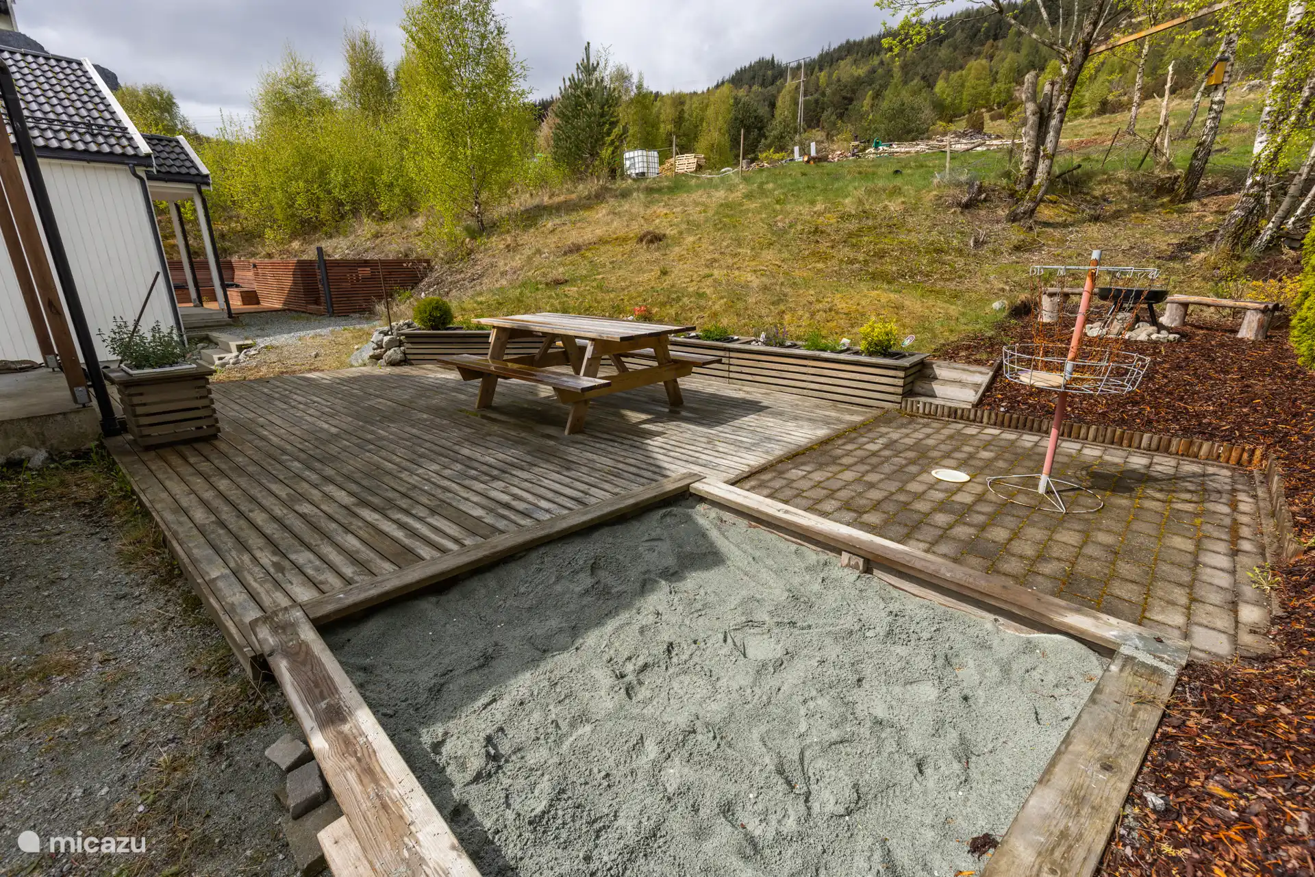 Le jardin privé derrière l’appartement comprend une terrasse avec un coin salon, un barbecue, un bac à sable et un panier à frisbee. 
