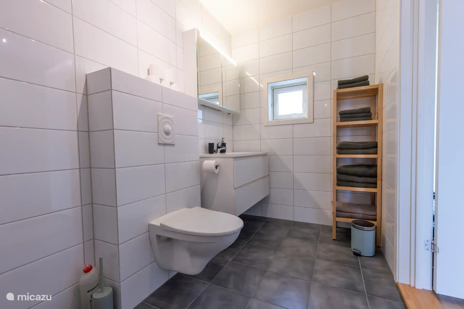 La salle de bain est spacieuse et lumineuse, avec un design moderne et minimaliste. La chambre est équipée d’une douche à l’italienne, d’un lavabo suspendu, d’un lavabo avec armoire miroir et d’un porte-serviettes ouvert.