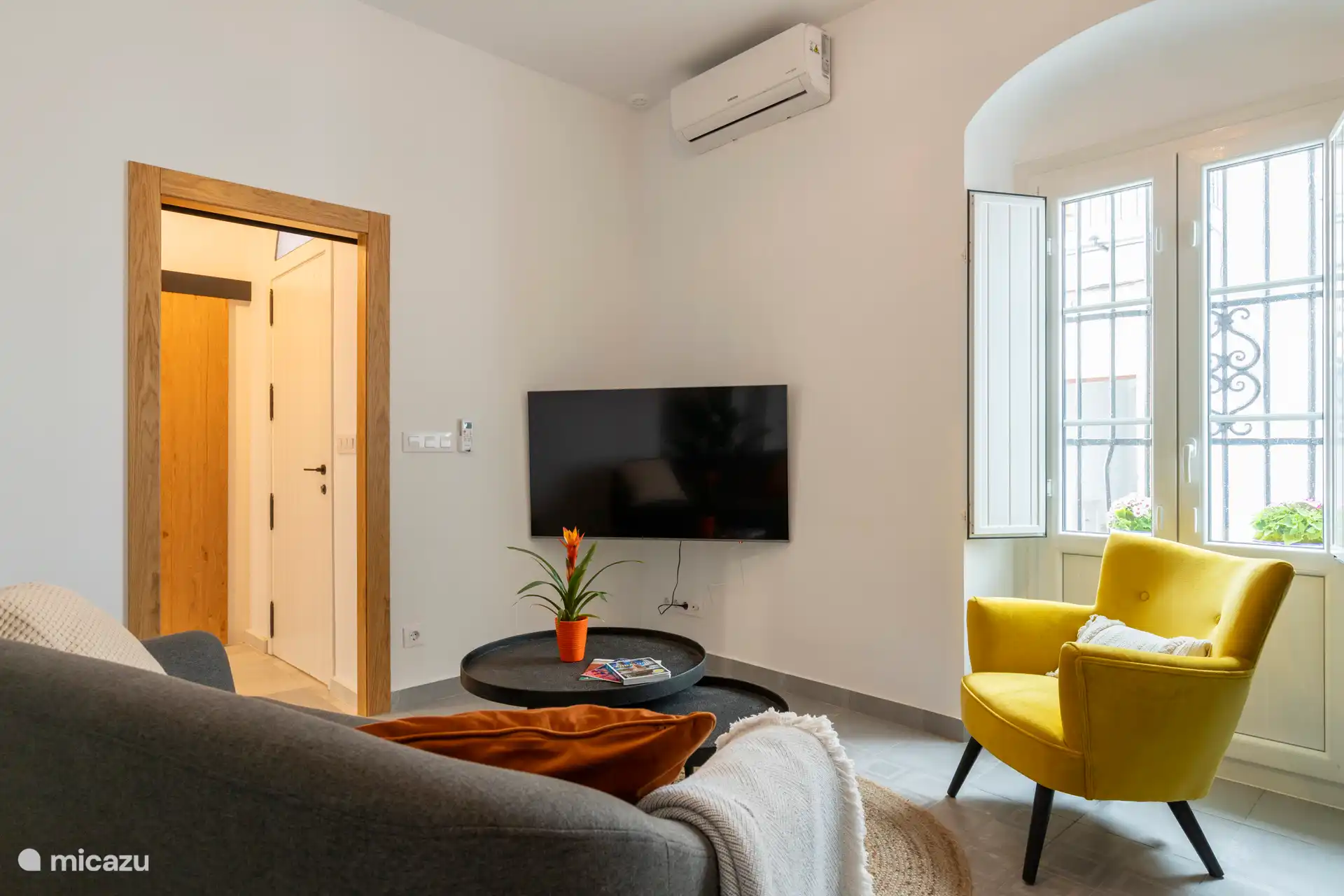 Geräumiges Wohnzimmer mit 2-Personen-Sofa, Fateuil, Arbeitstisch mit Hochstuhl, TV und Klimaanlage/Heizung. 