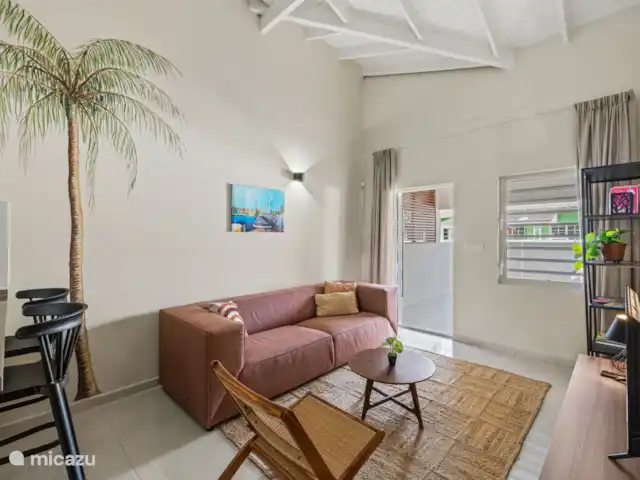 Bunita den Bario Apartments - A | Curaçao, Curaçao-Centre, Willemstad - maison de vacances Salon élégant avec un joli canapé 3 places, une Smart TV, une étagère avec des livres et des jeux de société.