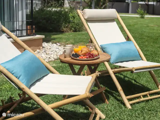 Location de Vacances Espagne, Costa del Sol, Estepona, appartement - Front de mer - Costa y Sol Deux chaises longues dans le jardin avec une table et des fruits frais