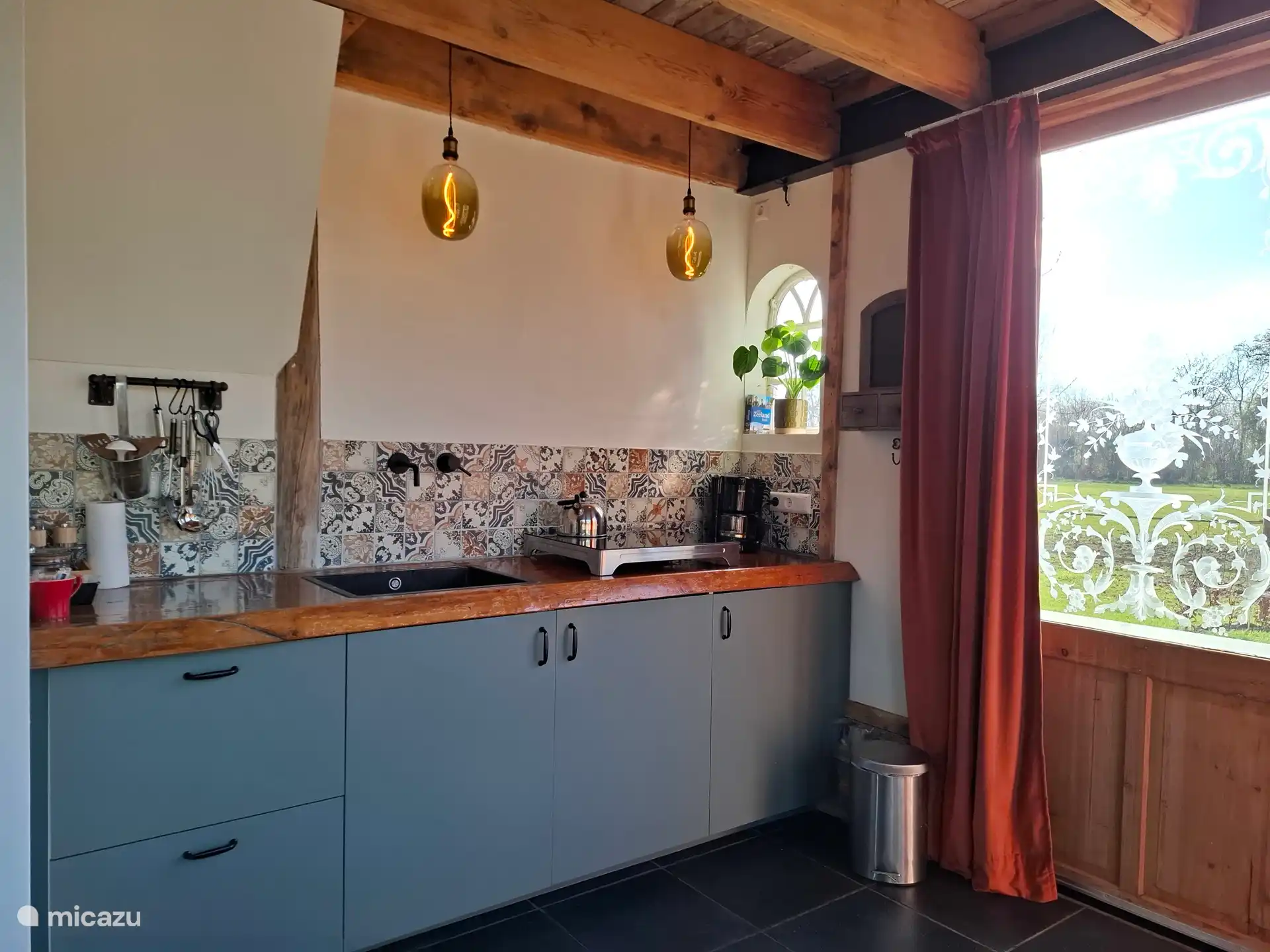 Küche mit Induktionskochfeld, Filterkaffeemaschine, Wasserkocher, Kühlschrank und kleinem Backofen. 