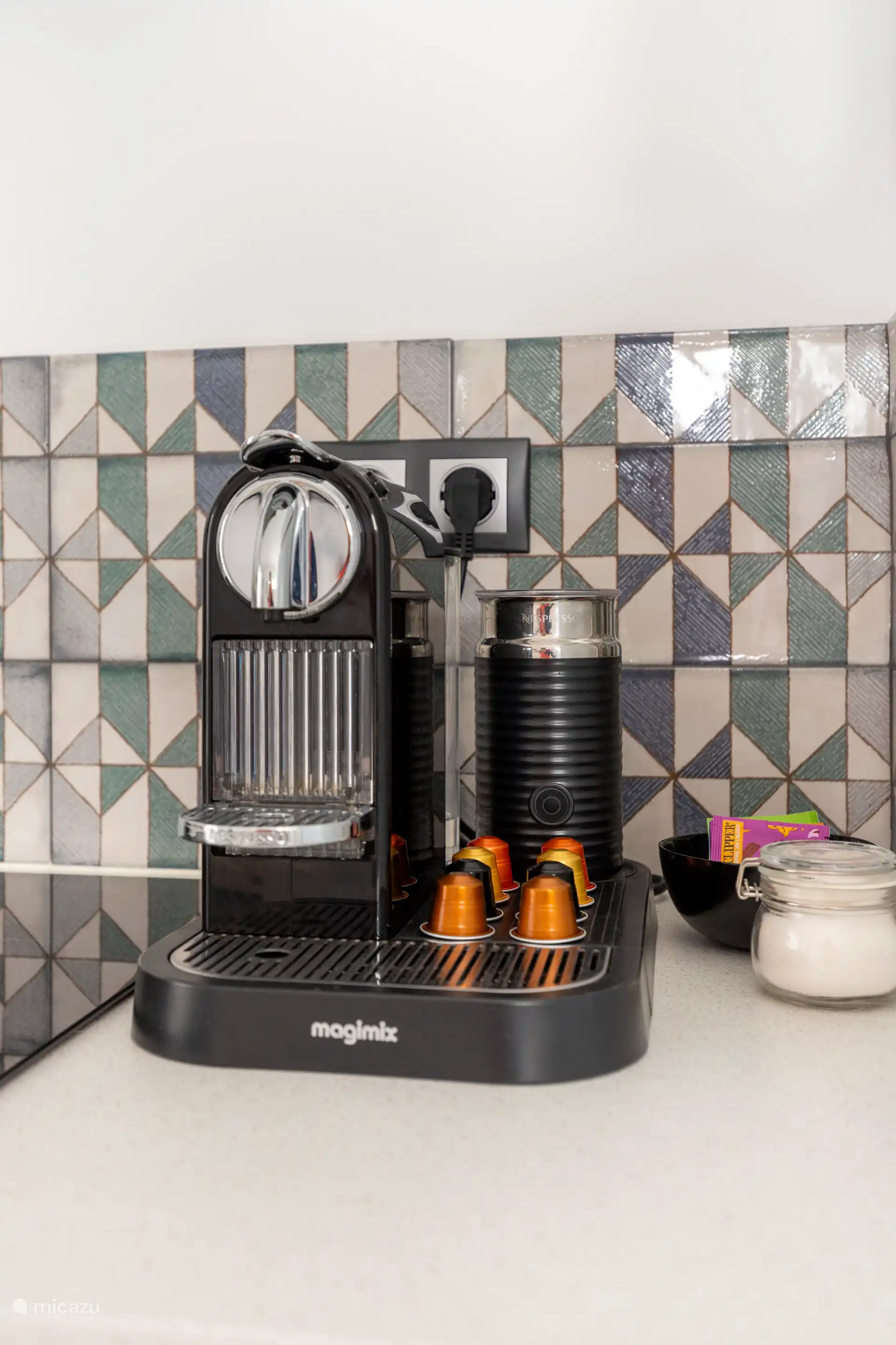 Cuisine entièrement équipée avec un réfrigérateur, un micro-ondes/grill, une plaque à induction, une machine à café Nespresso, un grille-pain SMEG, une bouilloire et une table avec quatre chaises.