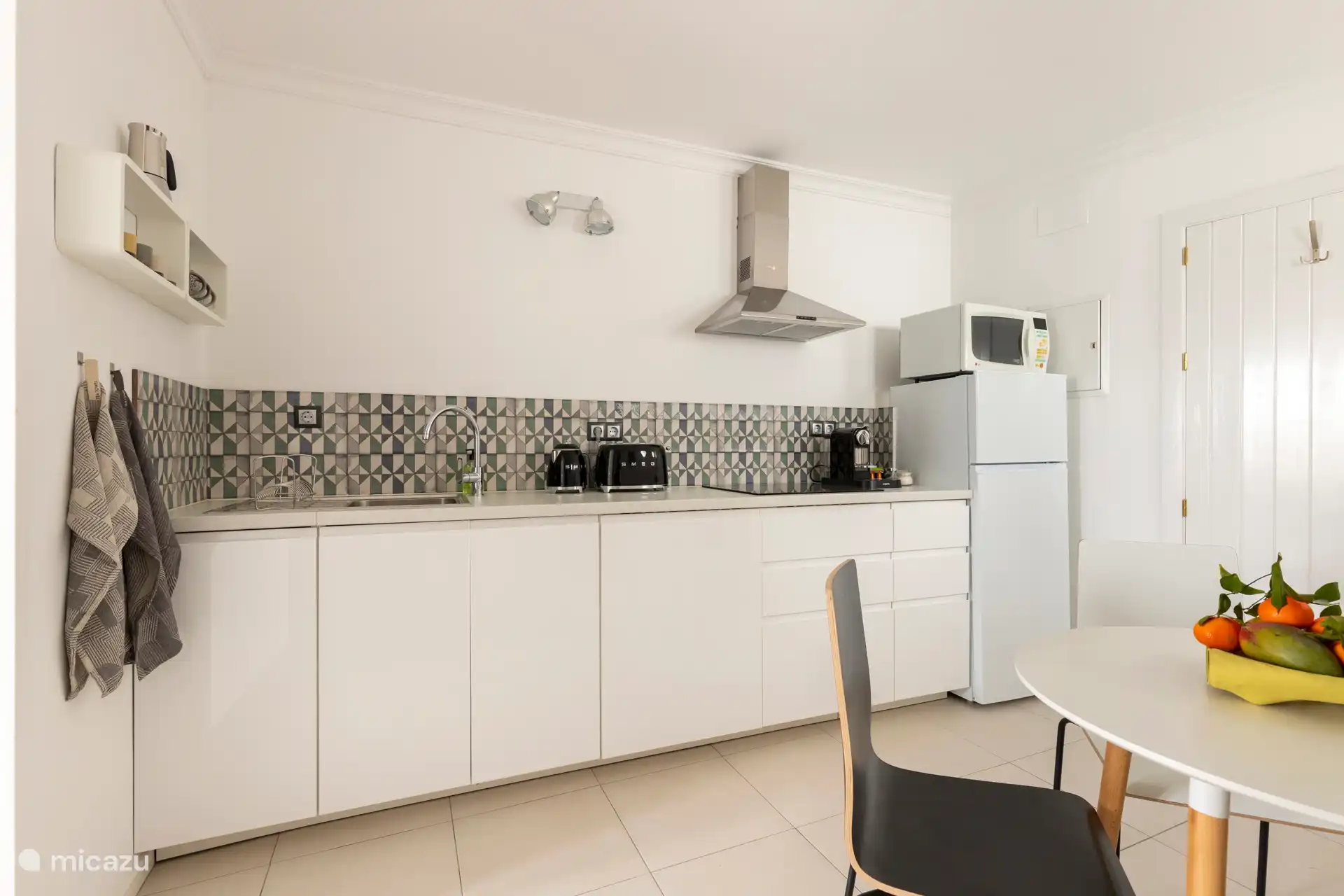 Cuisine entièrement équipée avec un réfrigérateur, un micro-ondes/grill, une plaque à induction, une machine à café Nespresso, un grille-pain SMEG, une bouilloire et une table avec quatre chaises.