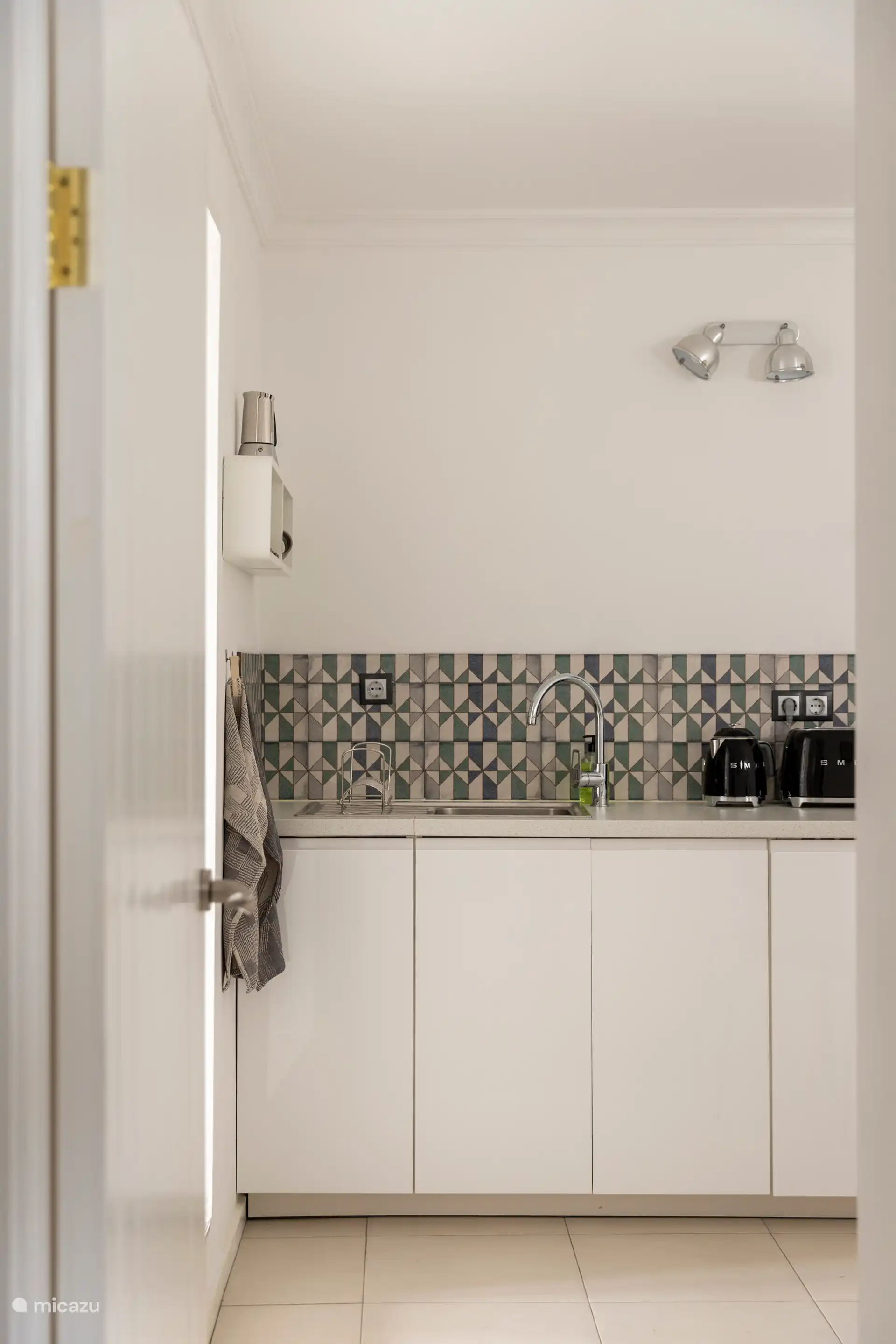 Cuisine entièrement équipée avec un réfrigérateur, un micro-ondes/grill, une plaque à induction, une machine à café Nespresso, un grille-pain SMEG, une bouilloire et une table avec quatre chaises.