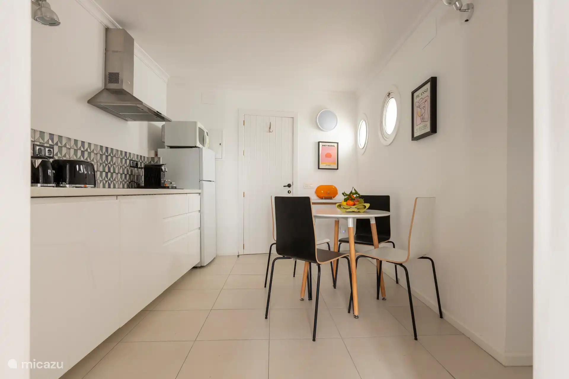 Cuisine entièrement équipée avec un réfrigérateur, un micro-ondes/grill, une plaque à induction, une machine à café Nespresso, un grille-pain SMEG, une bouilloire et une table avec quatre chaises.