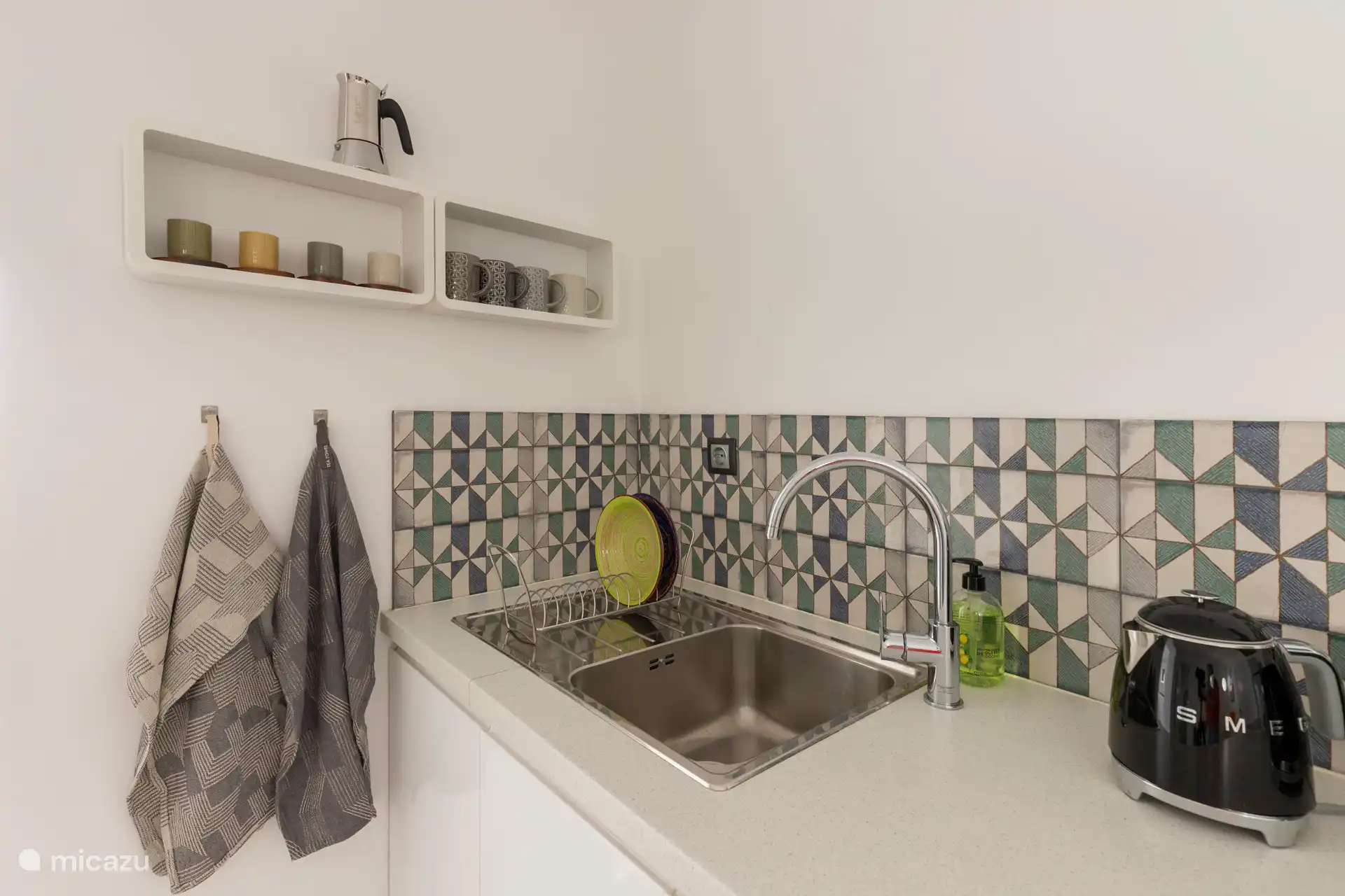 Cuisine entièrement équipée avec un réfrigérateur, un micro-ondes/grill, une plaque à induction, une machine à café Nespresso, un grille-pain SMEG, une bouilloire et une table avec quatre chaises.