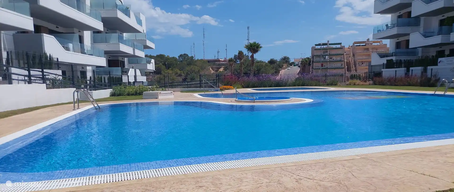 Blick auf das schöne Schwimmbad von der Liegewiese mit Liegestühlen und Sonnenschirmen