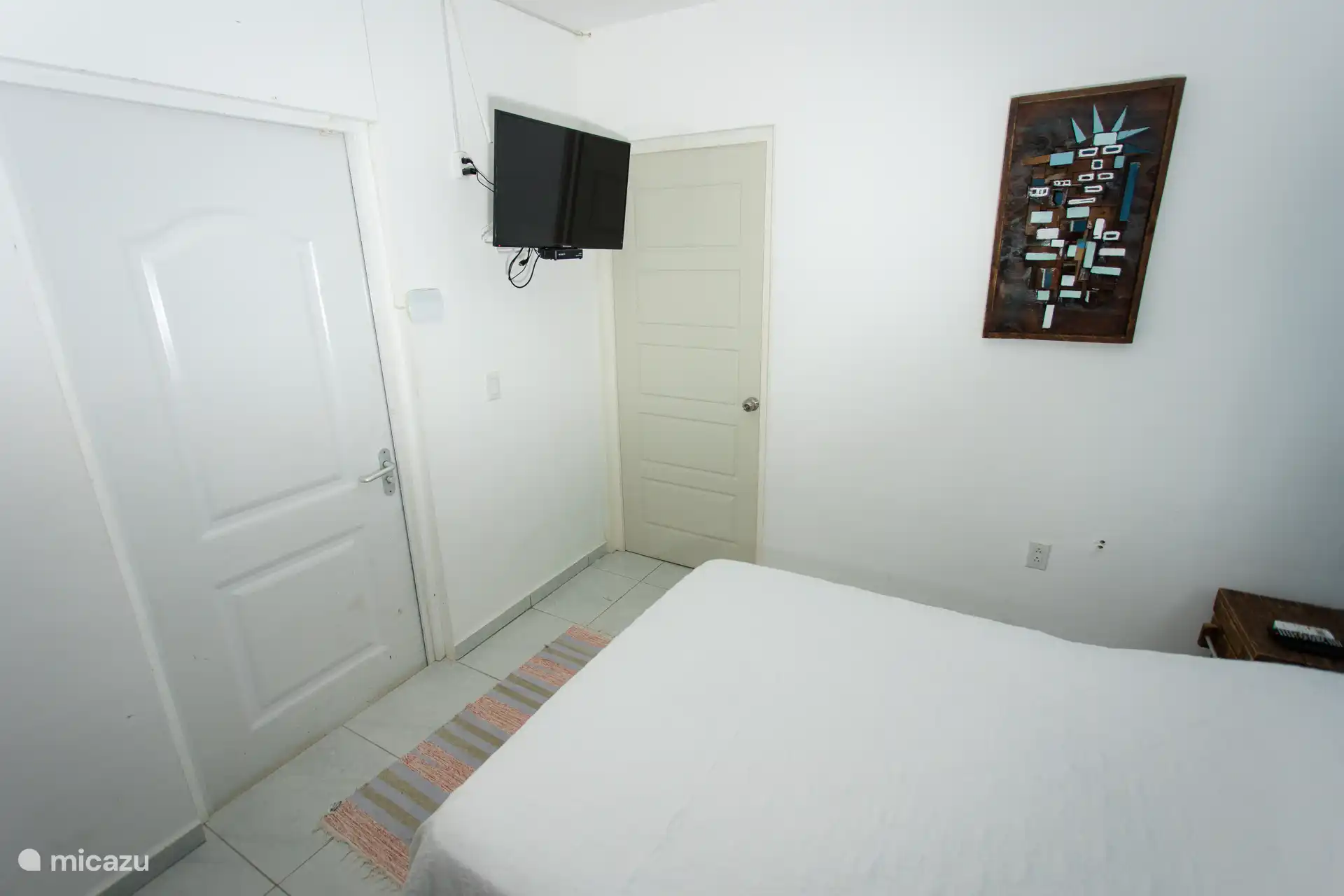 Gemütliches Schlafzimmer mit einem Doppelbett, weißer Bettwäsche, rustikalen Nachttischen und einem an der Wand montierten Smart-TV.