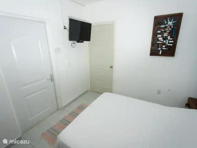 Studio Nature au bord de la piscine – Westpunt Es | Curaçao, Banda Abou (ouest), Westpunt - appartement Chambre confortable avec un lit double, des draps blancs, des tables de chevet rustiques et une télévision intelligente fixée au mur.