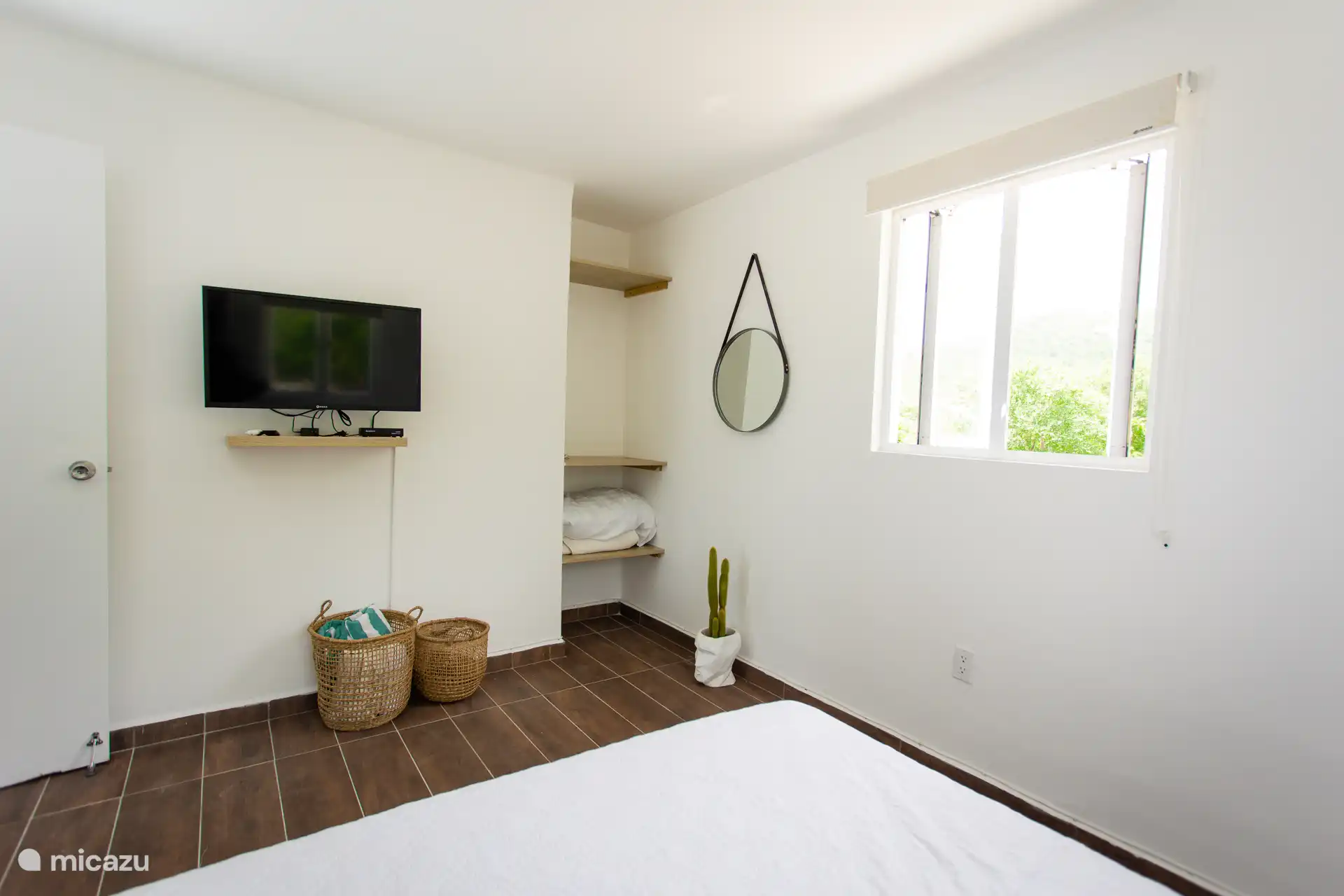 Functional and bright — the bedroom has open storage, a smart TV, and a large window for fresh light.