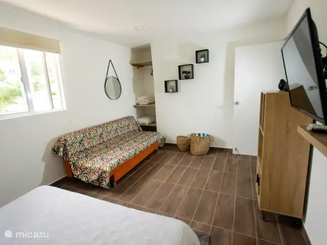 Retraite avec vue sur l’océan tropical | Curaçao, Banda Abou (ouest), Westpunt - appartement Vue secondaire de la chambre avec une télévision, un espace de rangement et un canapé-lit coloré.