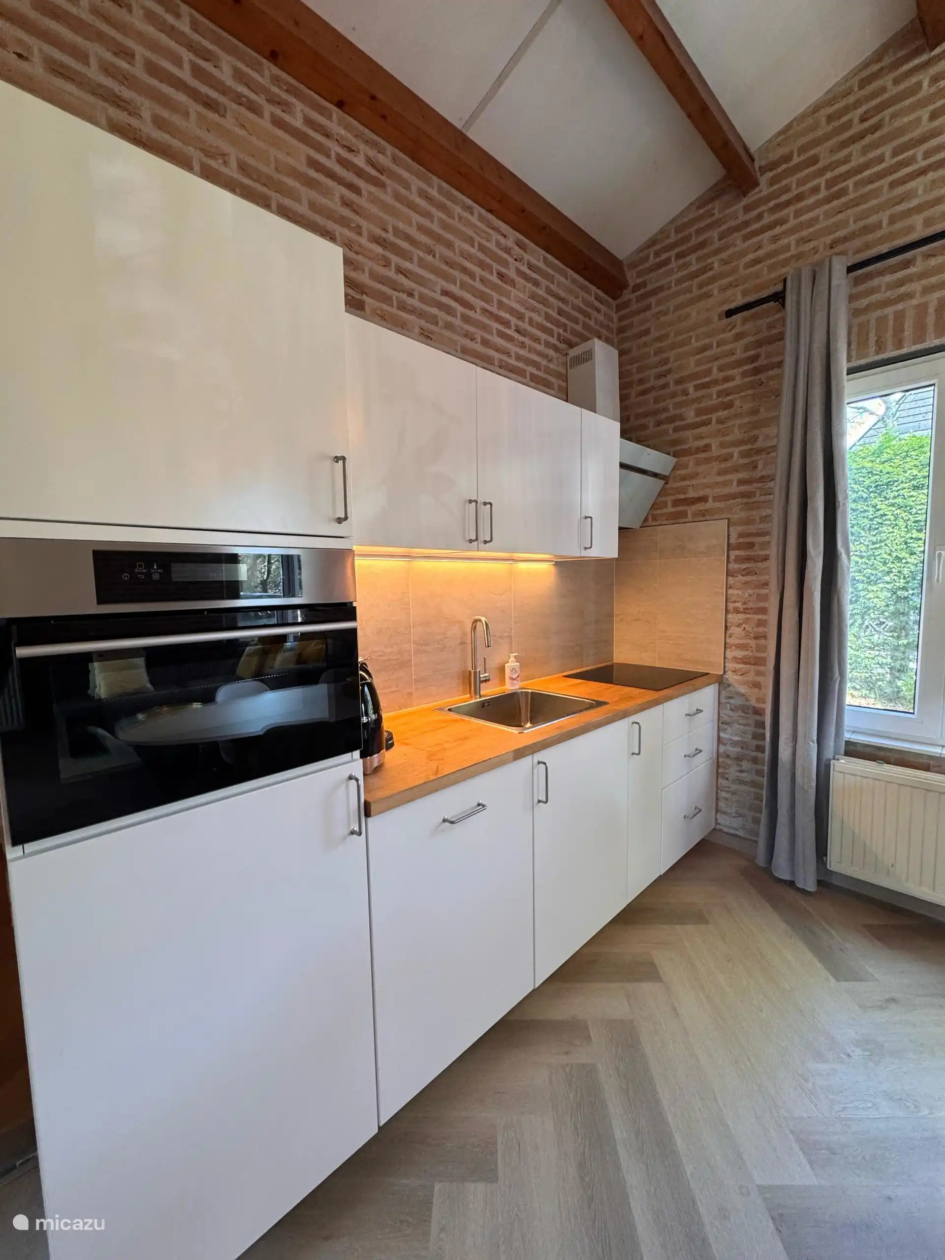 Elegante weiße Küche mit warmen Holzakzenten und Backsteinwand. Hier kann man auch im Urlaub genüsslich kochen.