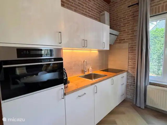Villa Frans | Pays-Bas, Zélande, Renesse - maison de vacances Cuisine blanche élégante avec des accents de bois chaleureux et un mur de briques. Ici, vous pouvez cuisiner avec plaisir, même en vacances.