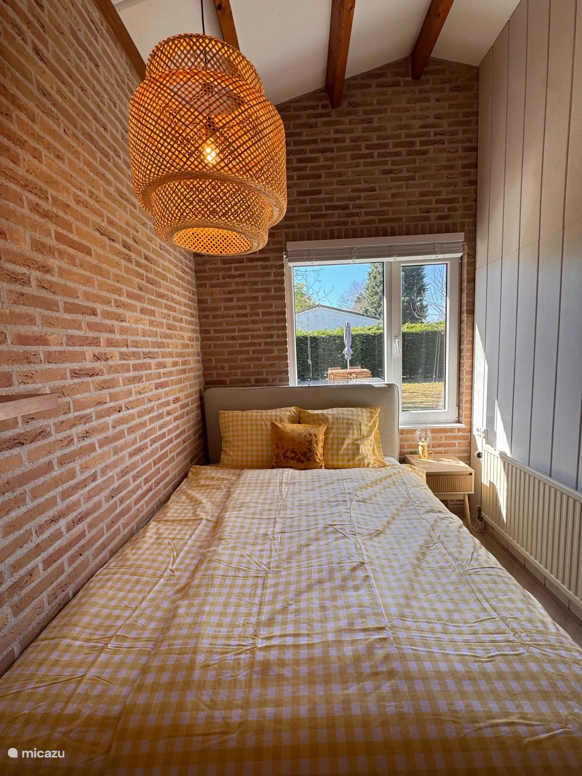 Gemütliche Schlafzimmerecke mit gelber und weißer Bettwäsche, Blick ins Grüne und einer sanften Morgensonne. Schlafen Sie gut in Zeeland!