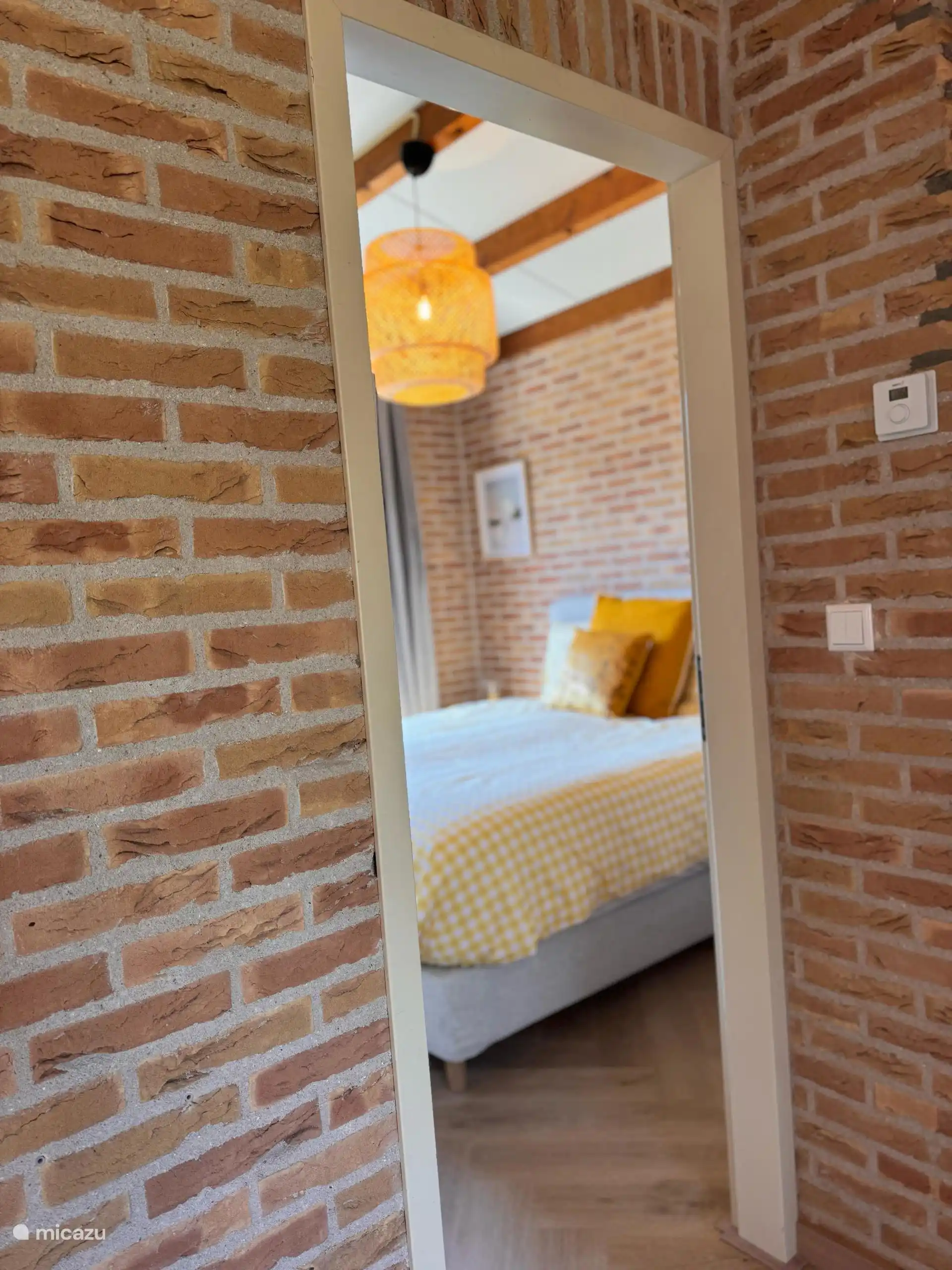 Ein Blick hindurch in ein gemütliches Schlafzimmer mit fröhlichen gelben Akzenten. Atmosphärisch, warm und einladend.