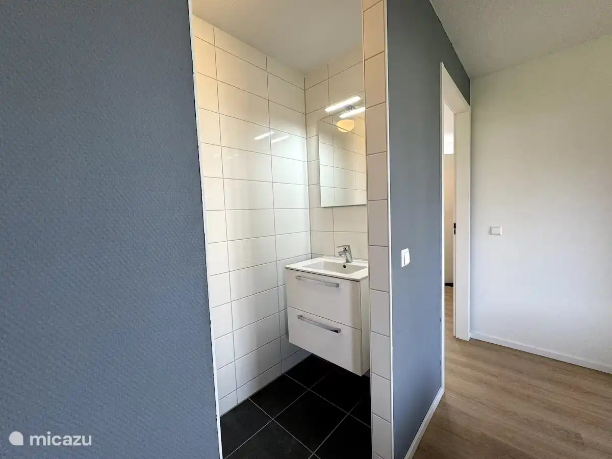 Frisse wastafelruimte met strakke lijnen en lichte tegels. De combinatie van zachte grijstinten en donker tegelwerk geeft de ruimte een moderne en rustige uitstraling.