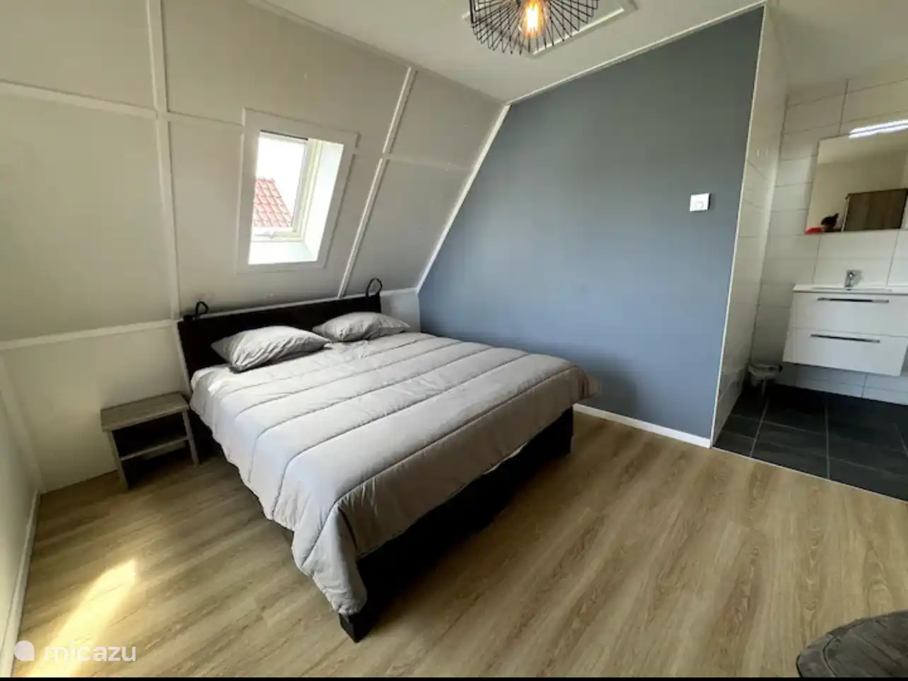 Rustige slaapkamer met zachte grijs en blauwtinten. Het dakraam laat natuurlijk licht binnenvallen terwijl de warme houtvloer en minimalistische styling zorgen voor een serene, ontspannen sfeer.