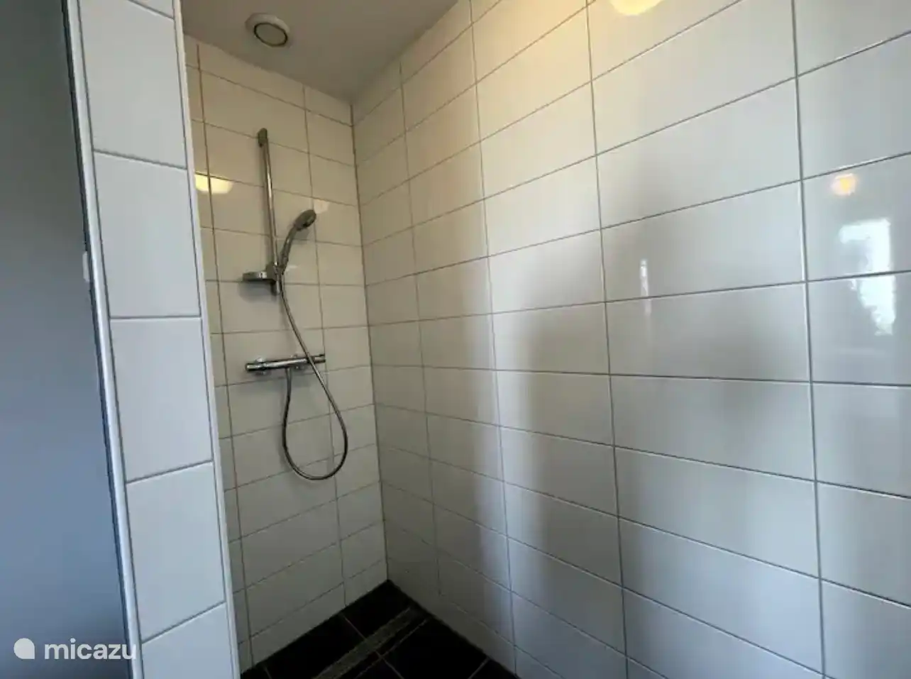 Ruime inloopdouche met frisse witte tegels en strak sanitair. De moderne afwerking en rustige kleuren zorgen voor een comfortabele plek om heerlijk te ontspannen.