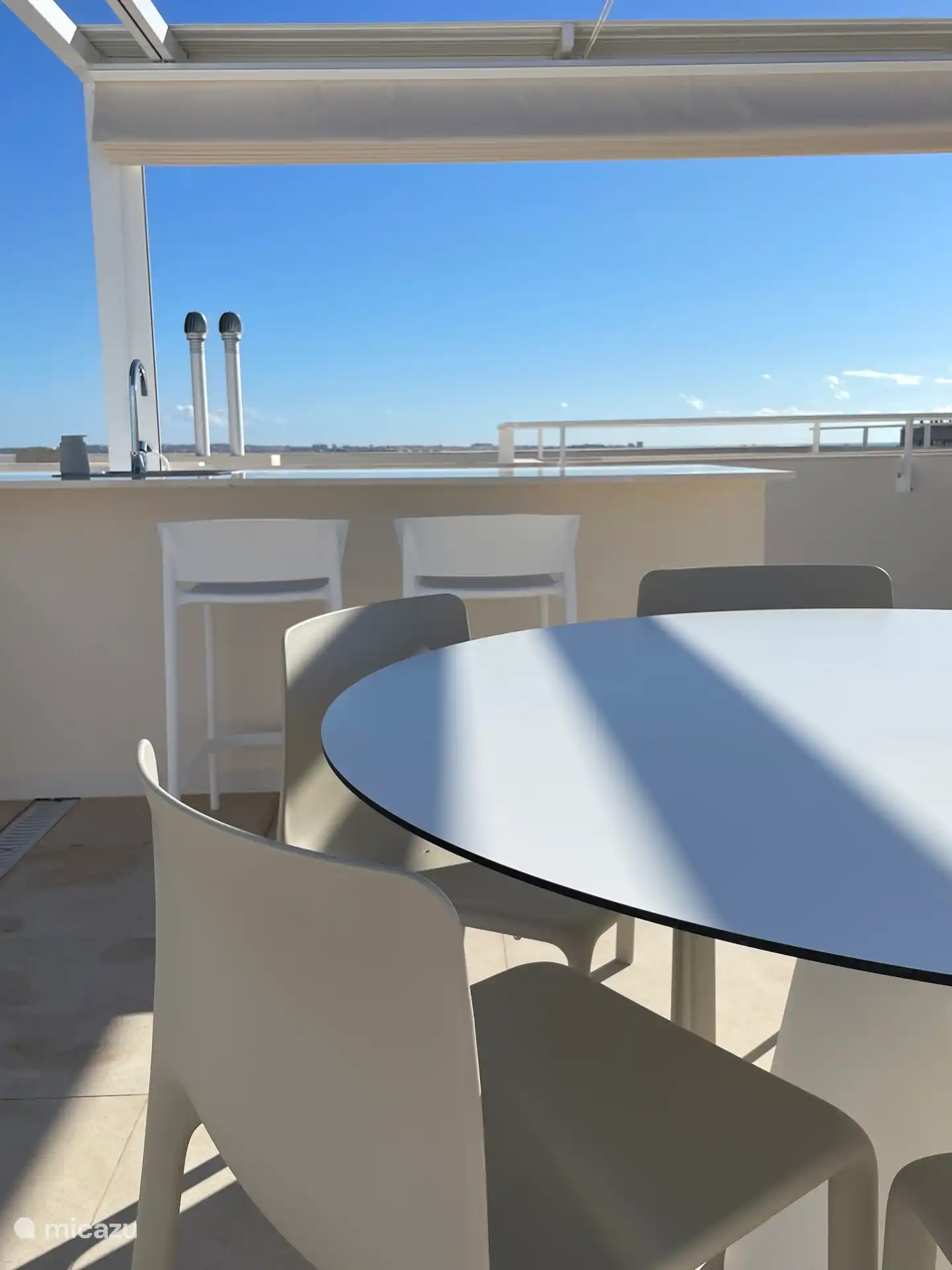 El solárium con mesa de comedor, taburetes de bar y la cocina exterior.