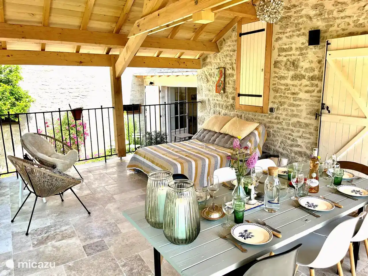 The terrace near the living room kitchen, with dining table, sunbed and seat with two chairs. In the background the entrance to the hall through large French doors.