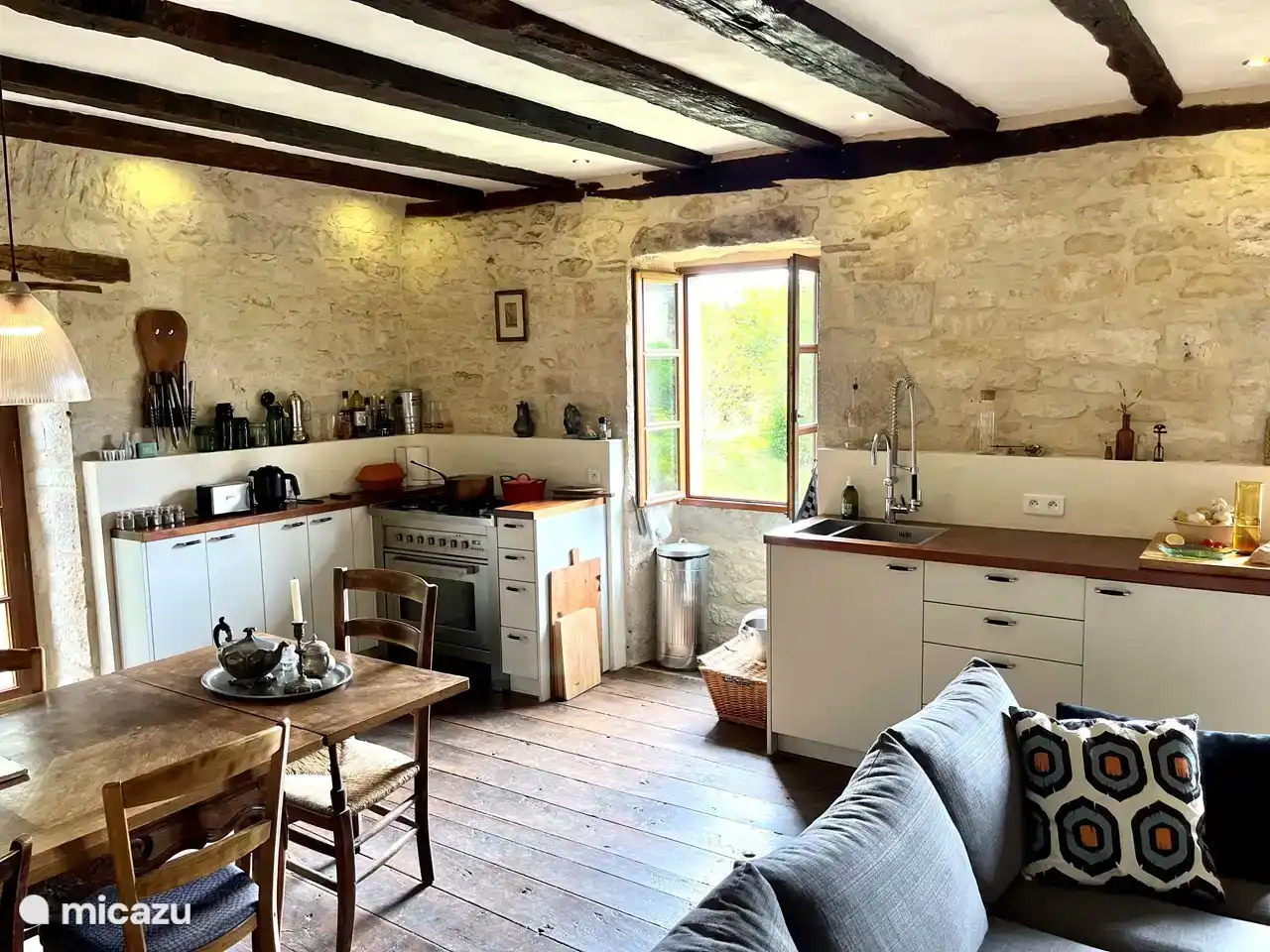 The kitchen/living room, with 5-burner stove, dining table and a piece of sofa. With windows all around to the garden and left to the road.