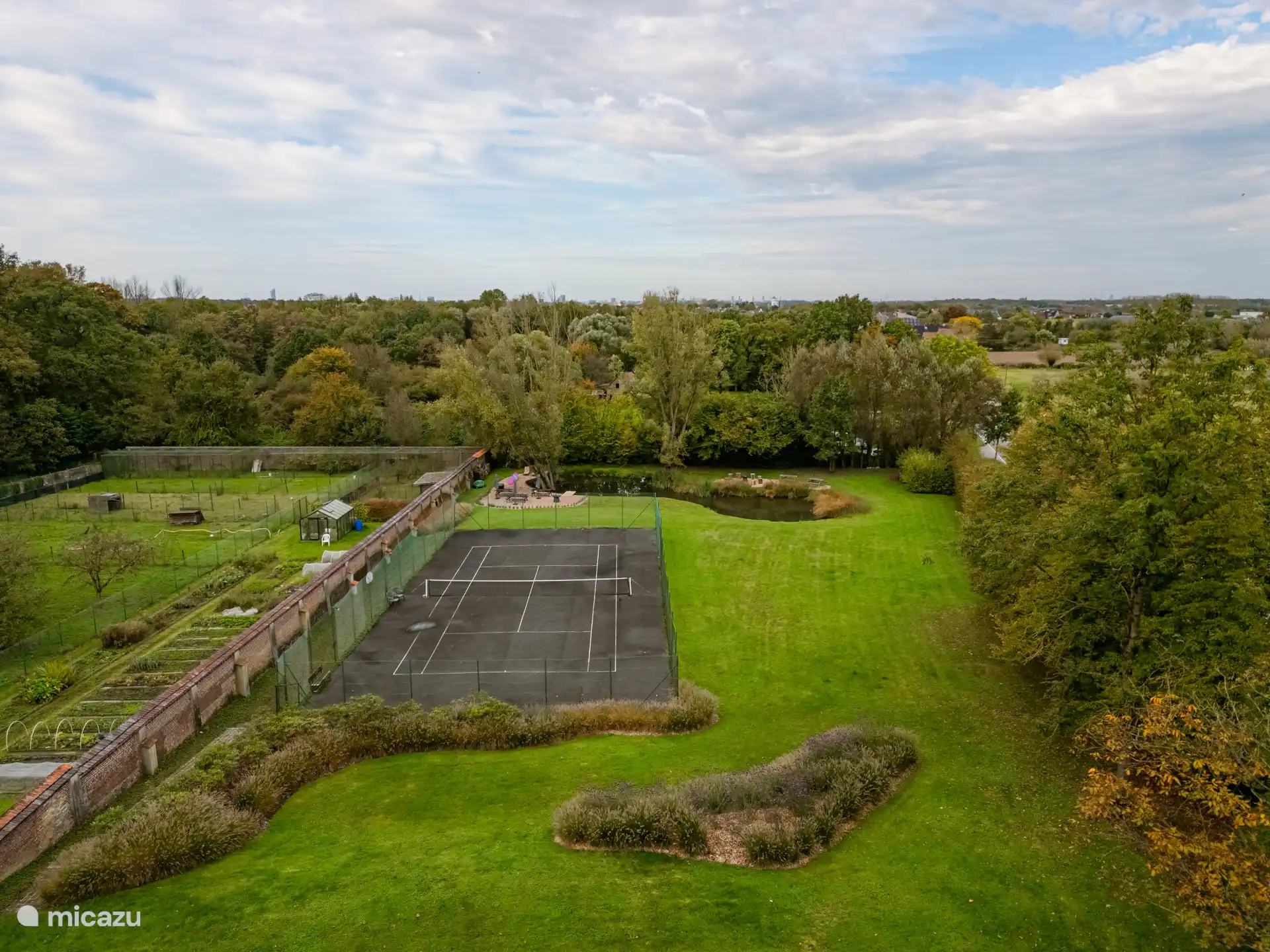 Blick auf das weitläufige Anwesen mit Tennisplatz und großem Teich.