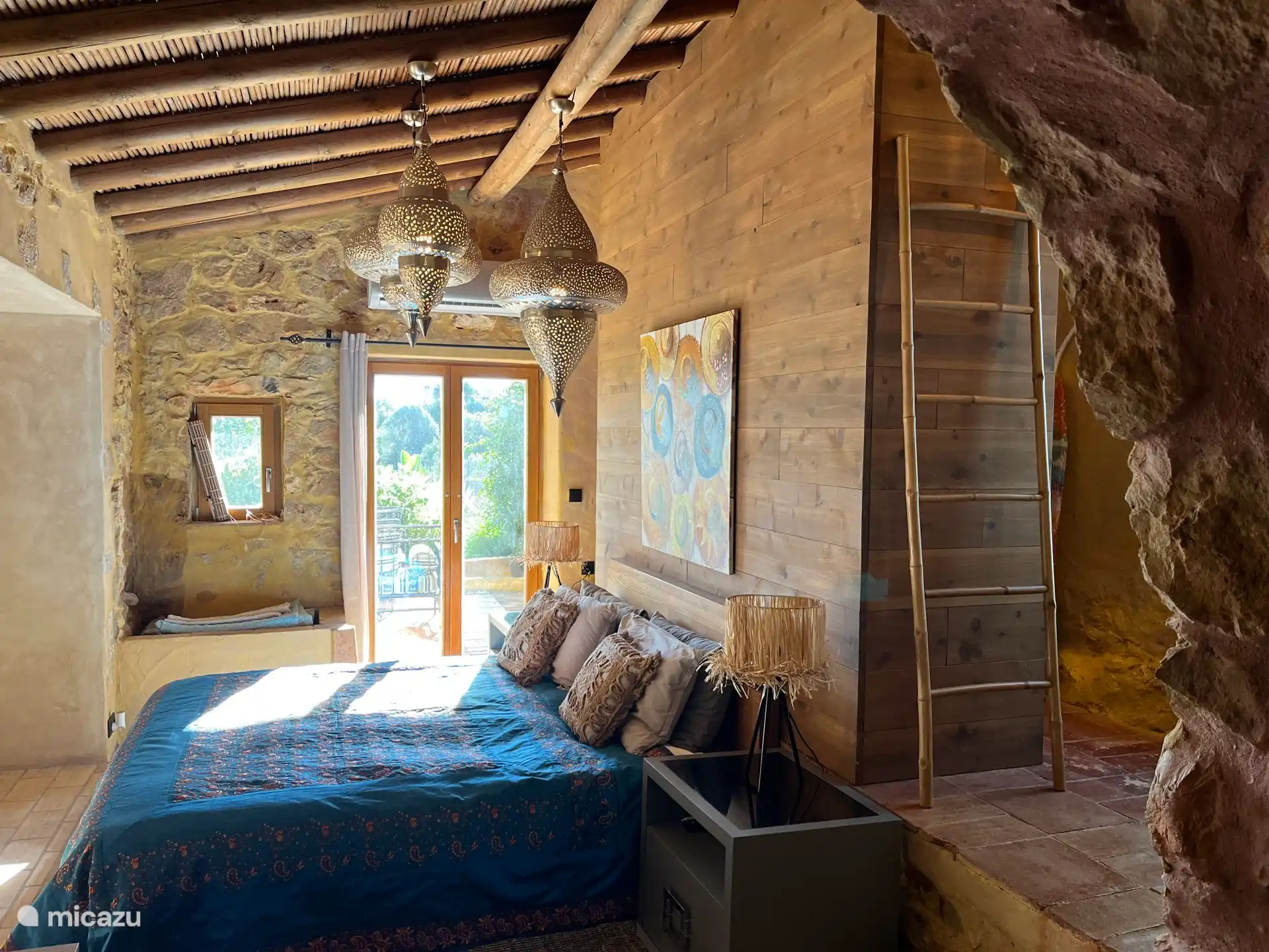 Hauptschlafzimmer mit französischen Türen zur Terrasse und Gartenmöbeln im marokkanischen Stil. Die begehbaren Einbauschränke sind hinter der Holzvertäfelung versteckt.