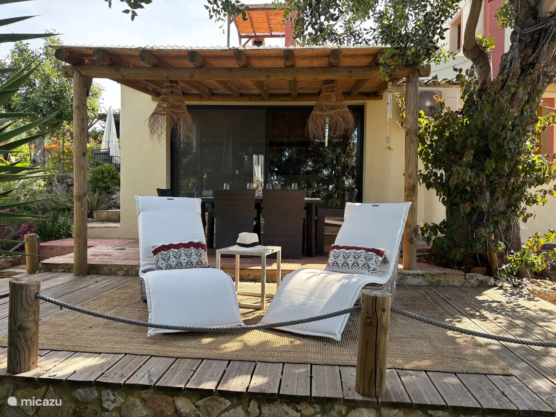 Sonnenliegen auf der Terrasse und Esstisch unter der überdachten Pergola