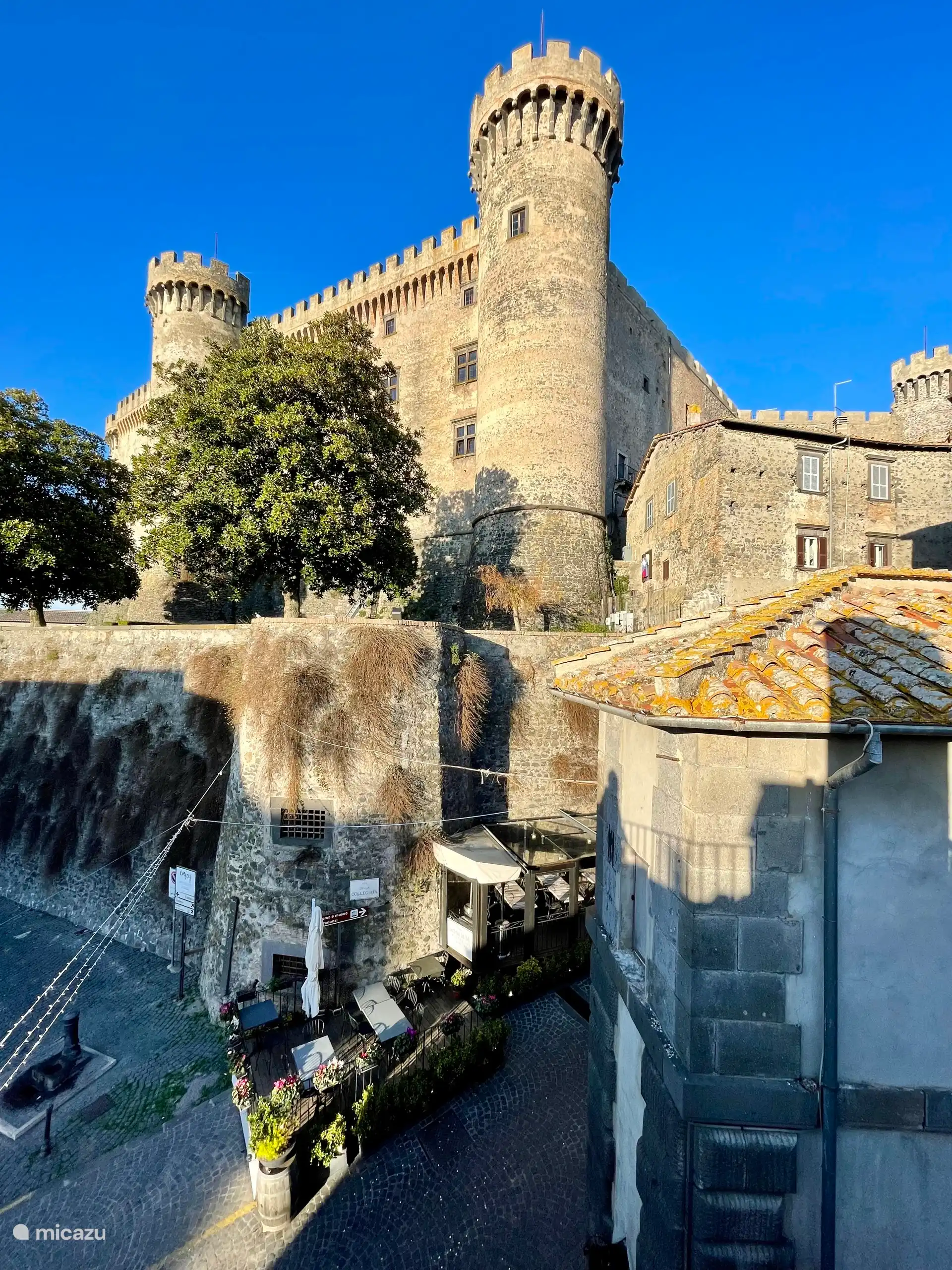 Atemberaubender Blick auf das Schloss Orsini-Odescalchi in Bracciano, das in der Sonne leuchtet. Ein majestätisches Wahrzeichen, das über dem Dorf thront, mit goldenen Dächern und einem kristallklaren blauen Himmel.