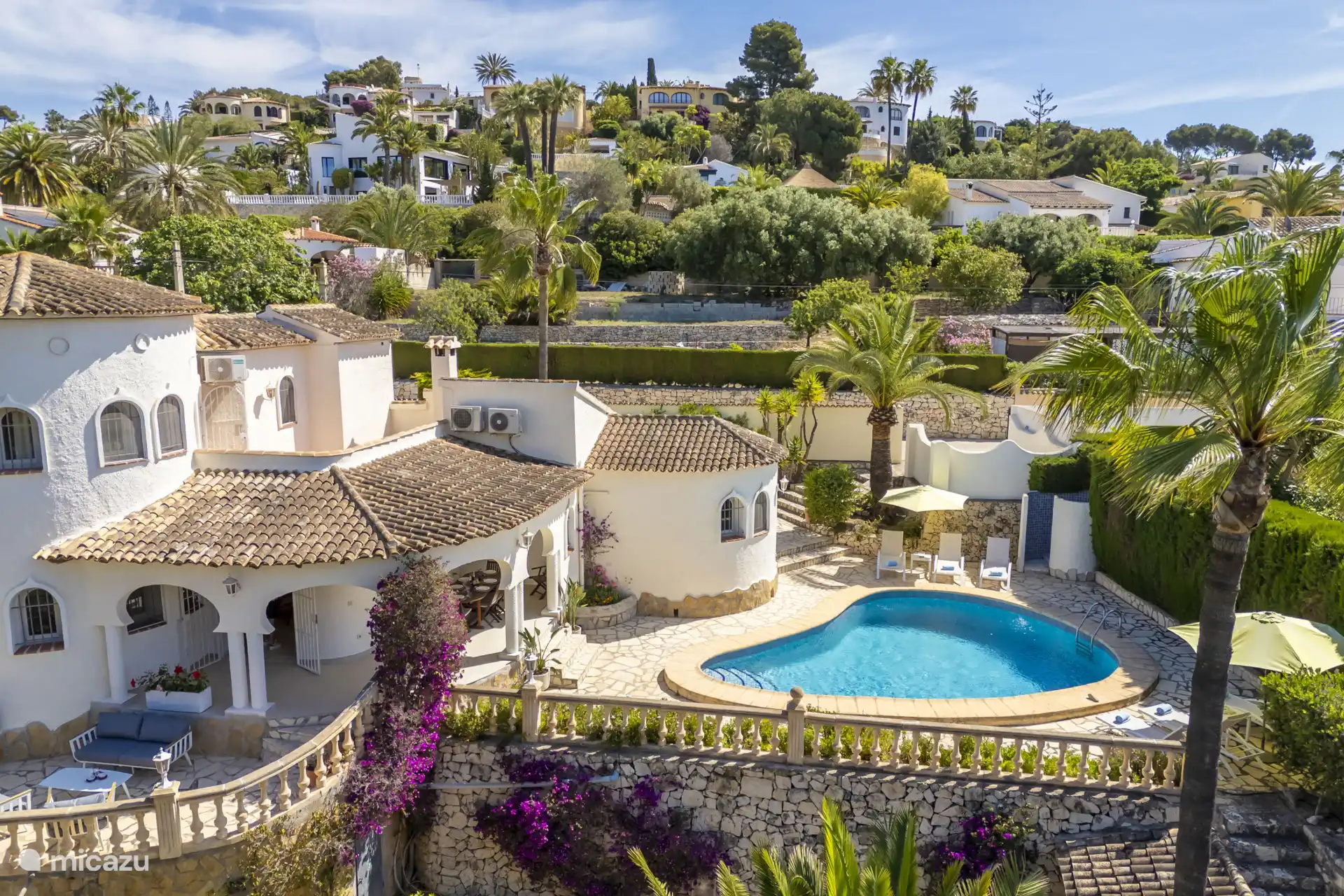 En medio del jardín se encuentra la piscina, rodeada de hamacas y sombrillas.