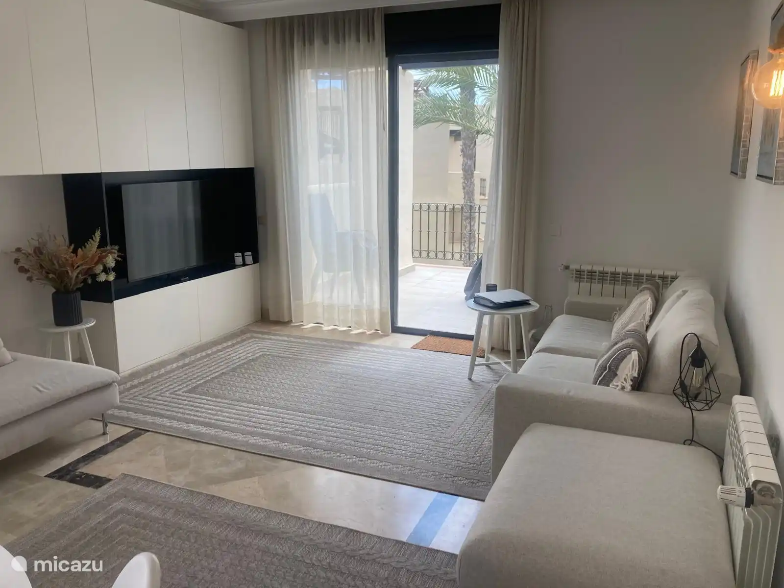 Das gemütliche Wohnzimmer verfügt über ein Sofa, einen bequemen Stuhl, eine Ottomane und einen Fernseher. Durch die Schiebetüren haben Sie Zugang zum Balkon. 