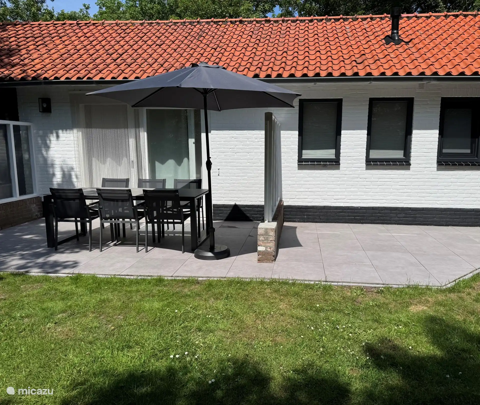 Nieuw aangelegd terras met links ruime tafelopstelling voor zes personen, parasol voor de ochtend schaduw en later op de dag deels natuurlijke schaduw erbij. Rechts extra zonneterras