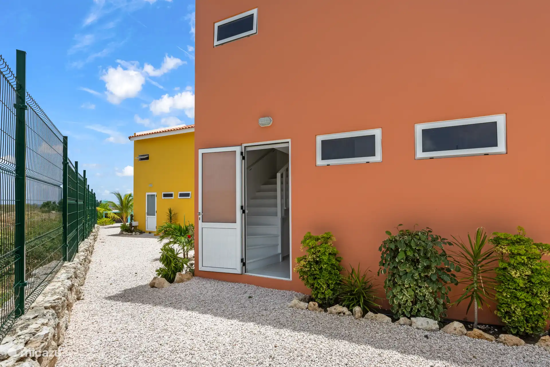 Die orangefarbene Fassade verleiht dem Haus ein warmes Aussehen, schön eingebettet in das umliegende Grün.