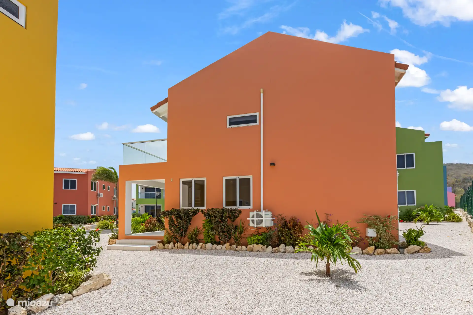 Die orangefarbene Fassade verleiht dem Haus ein warmes Aussehen, schön eingebettet in das umliegende Grün.