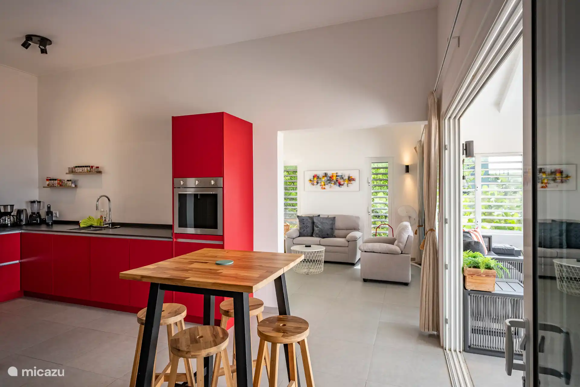 Eine moderne, voll ausgestattete Küche mit warmen Holzakzenten und Blick auf den hellen Wohnraum und die Lounge. Der ideale Ort, um gemeinsam zu kochen, etwas zu trinken und das tropische Inselgefühl zu genießen.