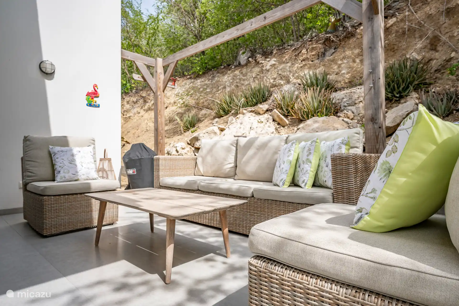 Eine attraktive Außenlounge mit bequemen Rattansitzen, fröhlichen Kissen und tropischem Grün. Wunderbar kühl am Nachmittag und perfekt zum Entspannen oder zum Zubereiten eines gemütlichen BBQs am Abend.