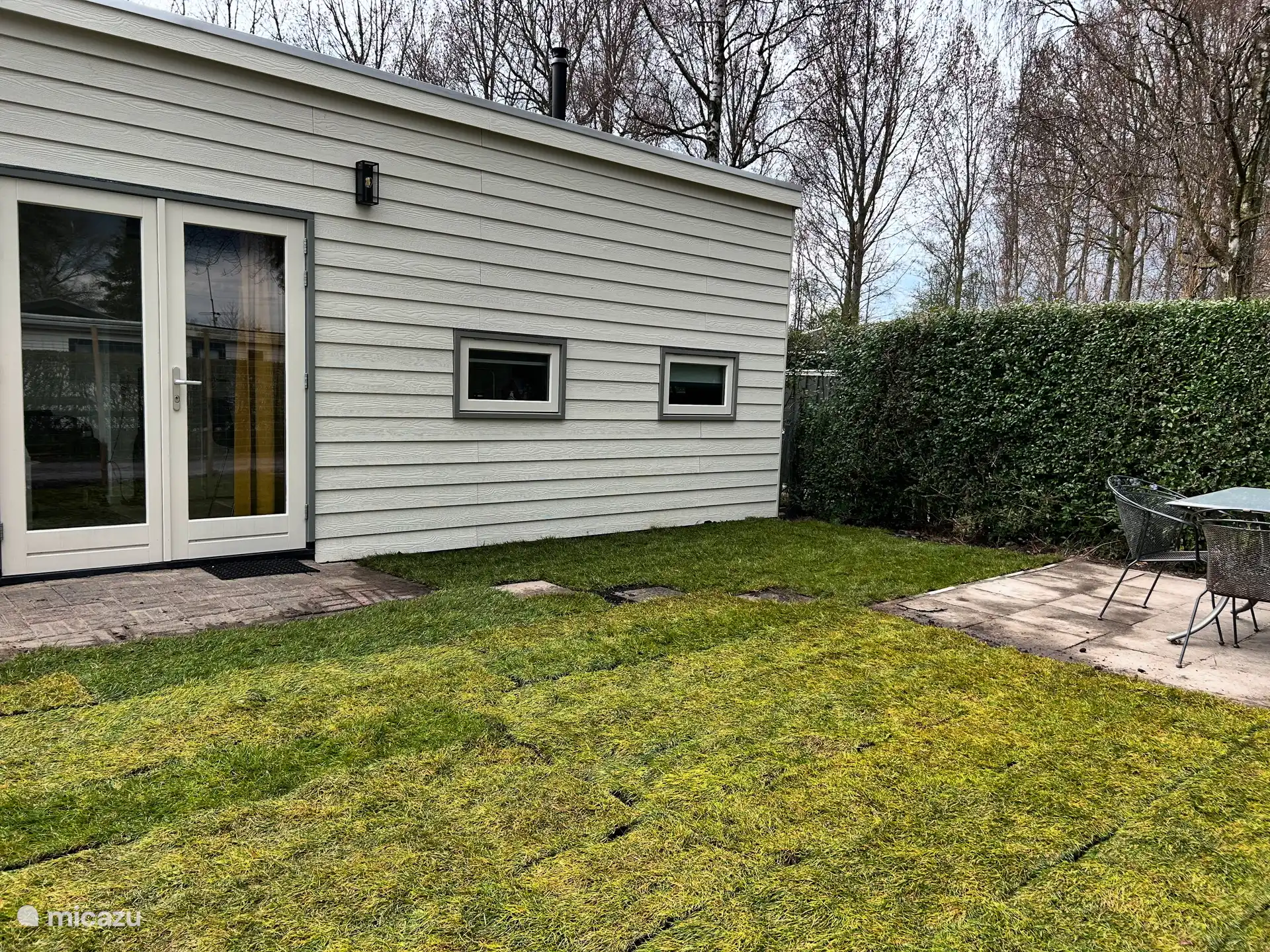 Vista frontal con césped y terraza con mesa de jardín.