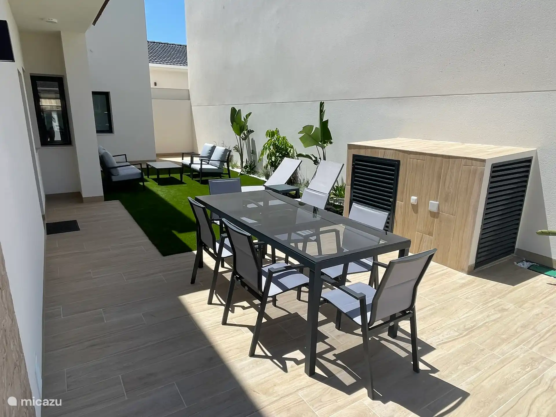 Zona exterior con mesa y 6 sillas, 2 tumbonas y un salón.